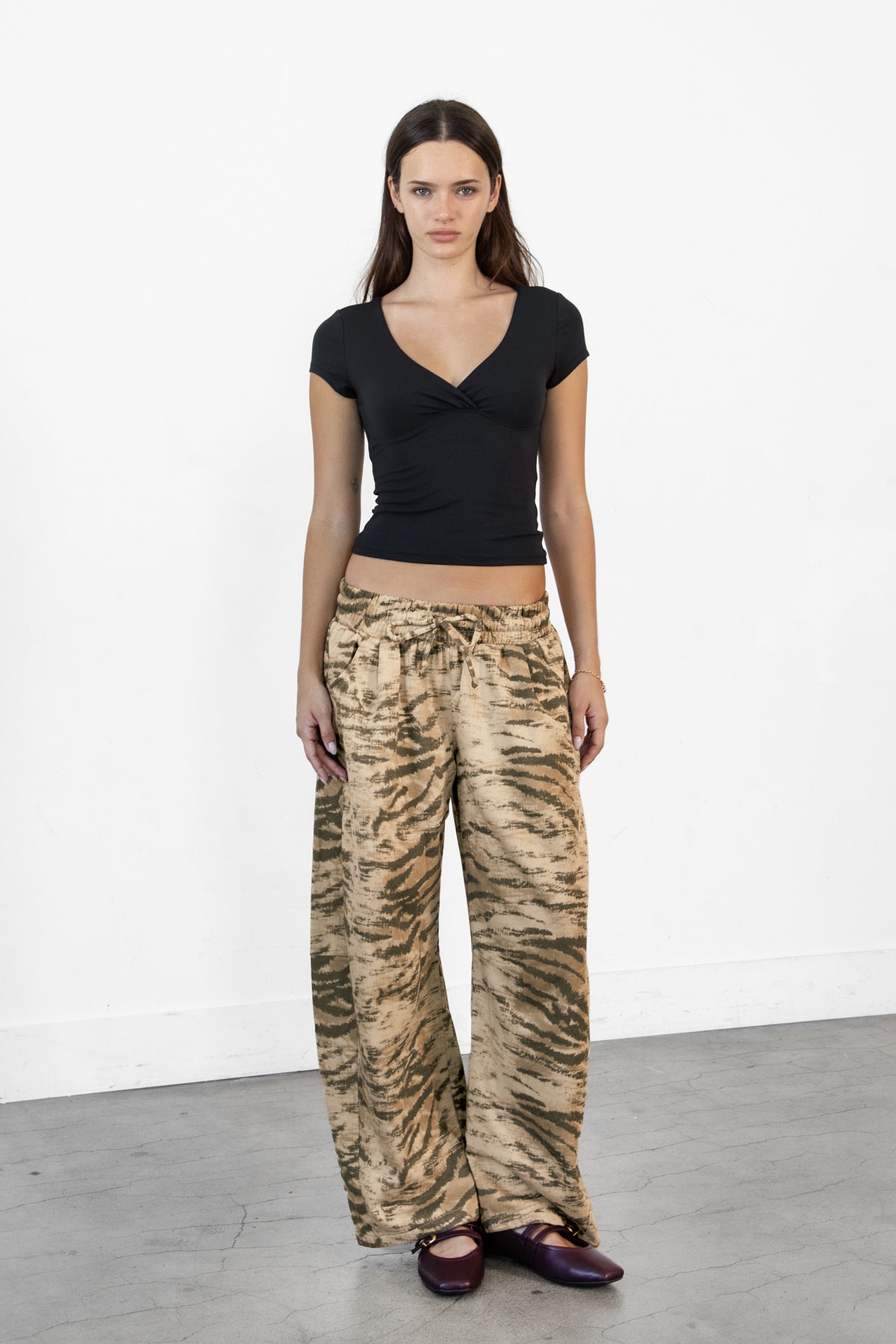 Woman wearing ZARIA tiger print wide leg pants featuring soft polyester cotton blend fabric, allover abstract tiger print in earthy beige, brown, and olive tones, elastic waistband with adjustable drawstring tie, relaxed fit through the hips and thighs, functional side pockets, wide leg silhouette with a subtle barrel shape, and full length design with paneled seam detailing.