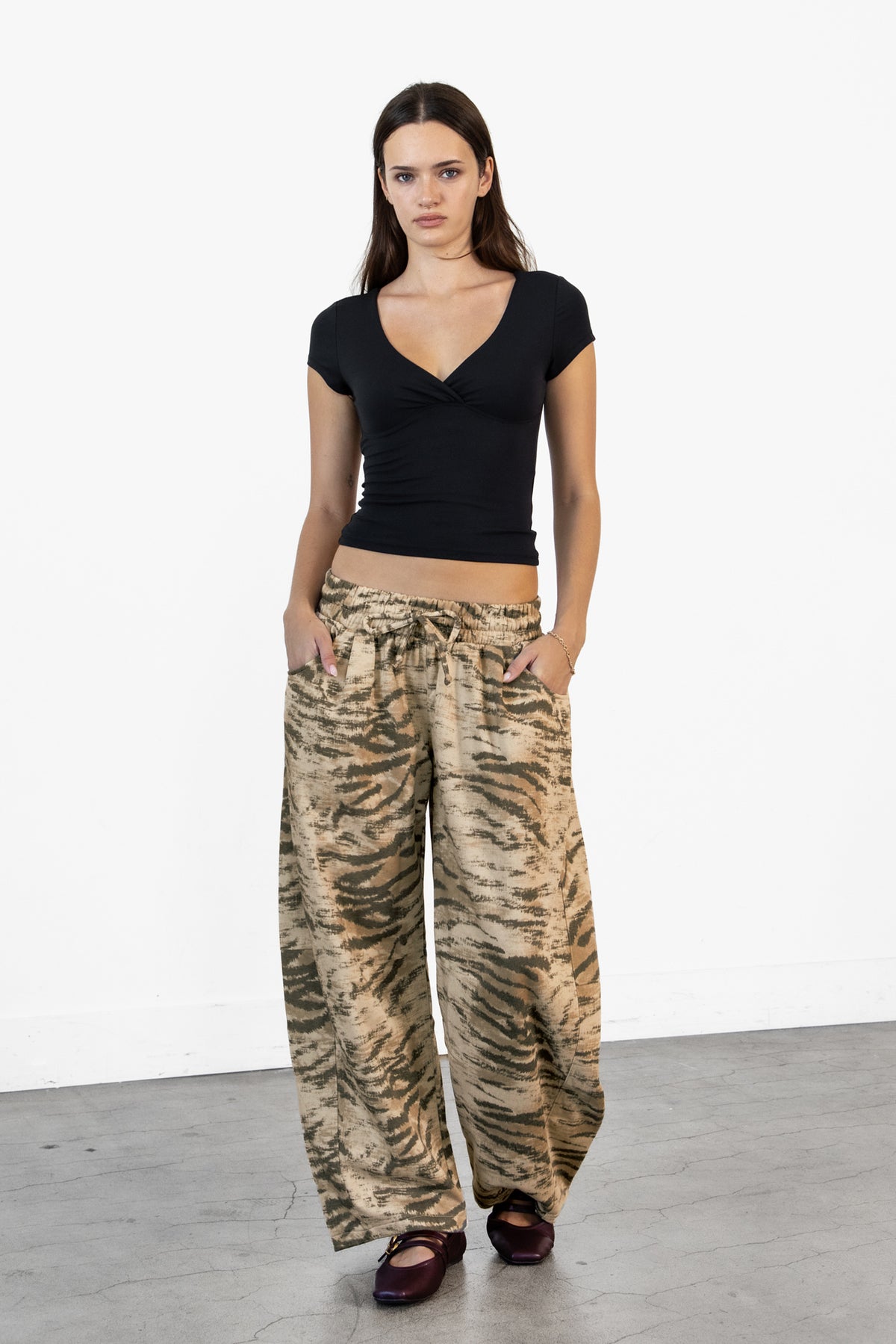 Woman wearing ZARIA tiger print wide leg pants featuring soft polyester cotton blend fabric, allover abstract tiger print in earthy beige, brown, and olive tones, elastic waistband with adjustable drawstring tie, relaxed fit through the hips and thighs, functional side pockets, wide leg silhouette with a subtle barrel shape, and full length design with paneled seam detailing.