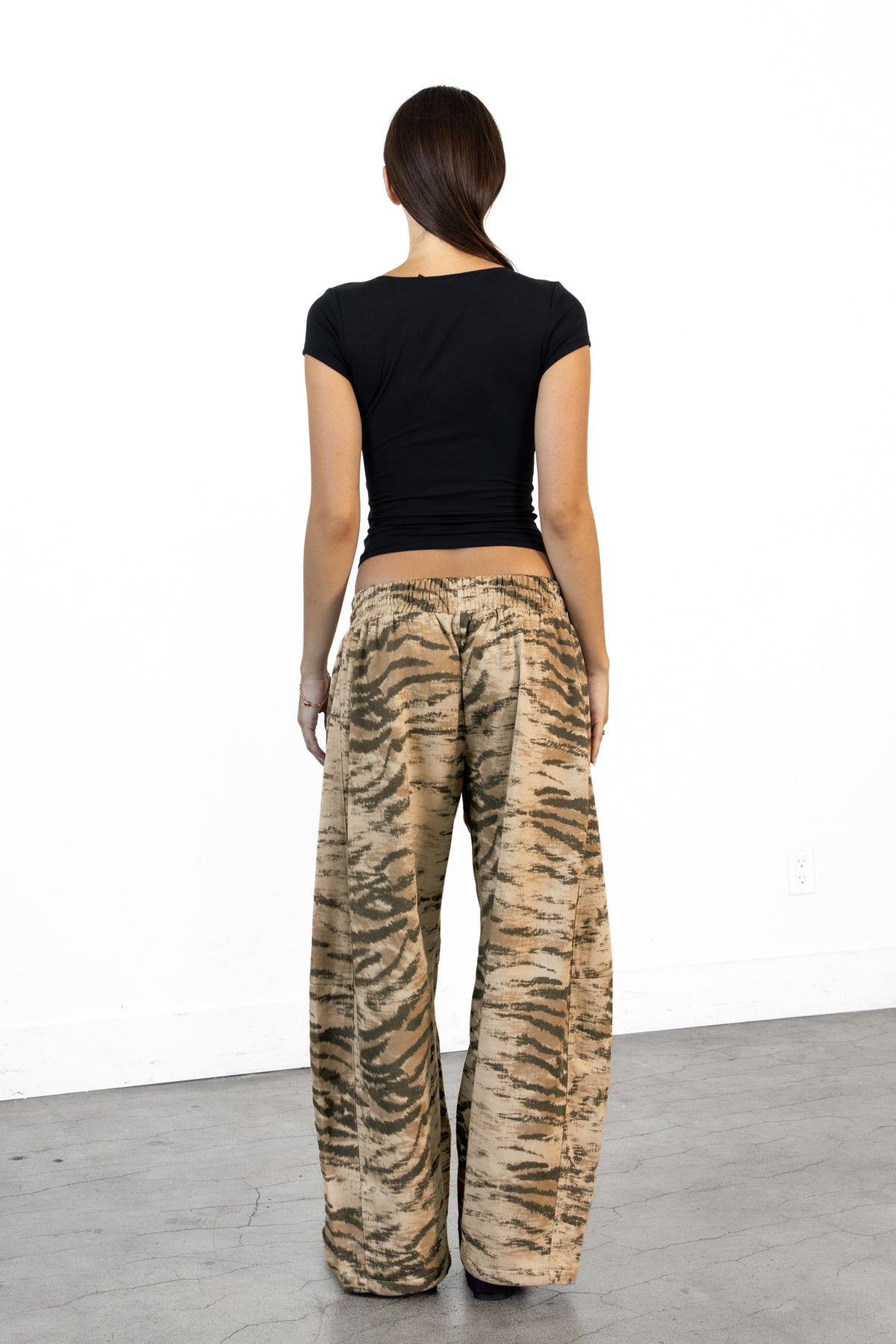 Woman wearing ZARIA tiger print wide leg pants featuring soft polyester cotton blend fabric, allover abstract tiger print in earthy beige, brown, and olive tones, elastic waistband with adjustable drawstring tie, relaxed fit through the hips and thighs, functional side pockets, wide leg silhouette with a subtle barrel shape, and full length design with paneled seam detailing.