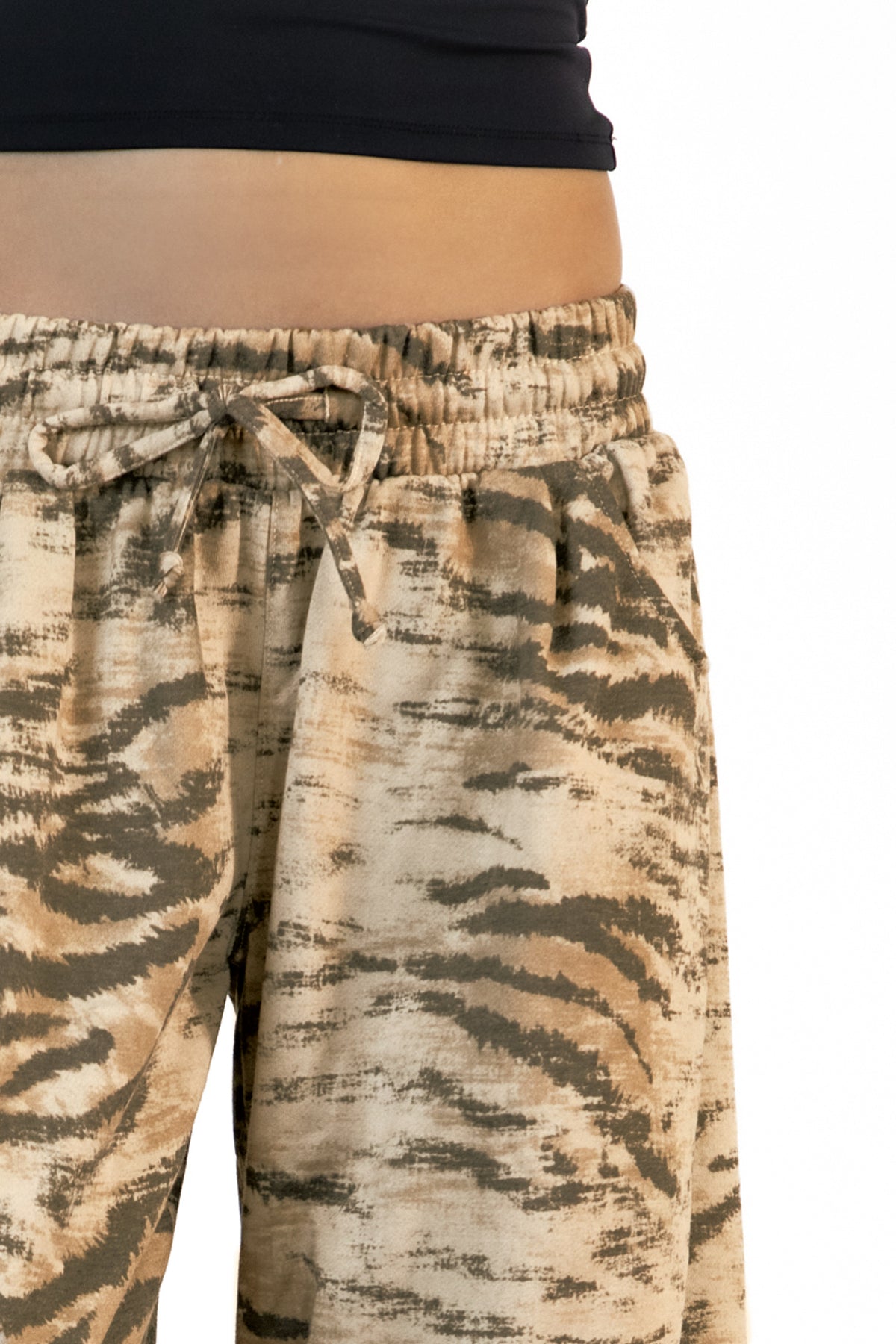 Woman wearing ZARIA tiger print wide leg pants featuring soft polyester cotton blend fabric, allover abstract tiger print in earthy beige, brown, and olive tones, elastic waistband with adjustable drawstring tie, relaxed fit through the hips and thighs, functional side pockets, wide leg silhouette with a subtle barrel shape, and full length design with paneled seam detailing.