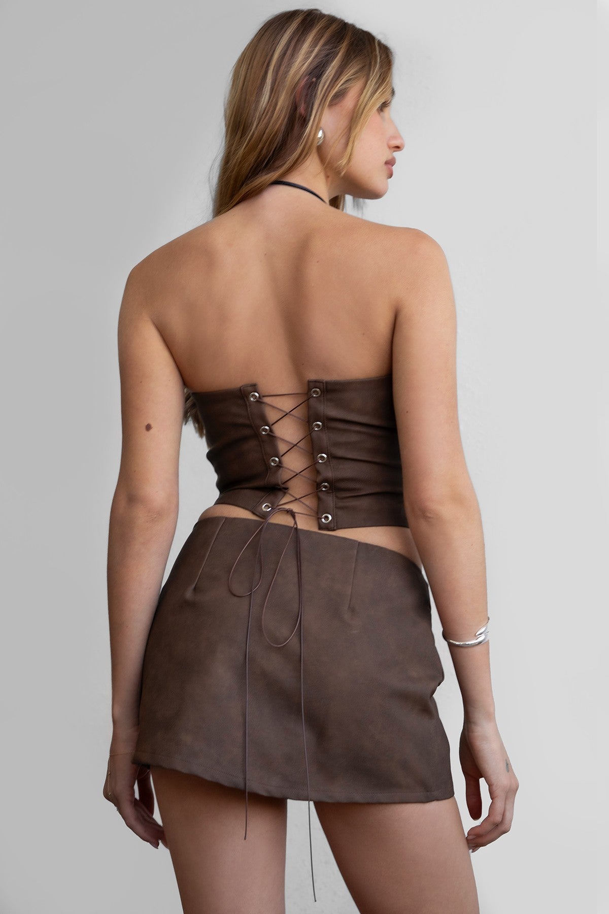 A woman wearing a brown strapless corset top with embroidered western-style details and a straight neckline, paired with a brown mini skirt.