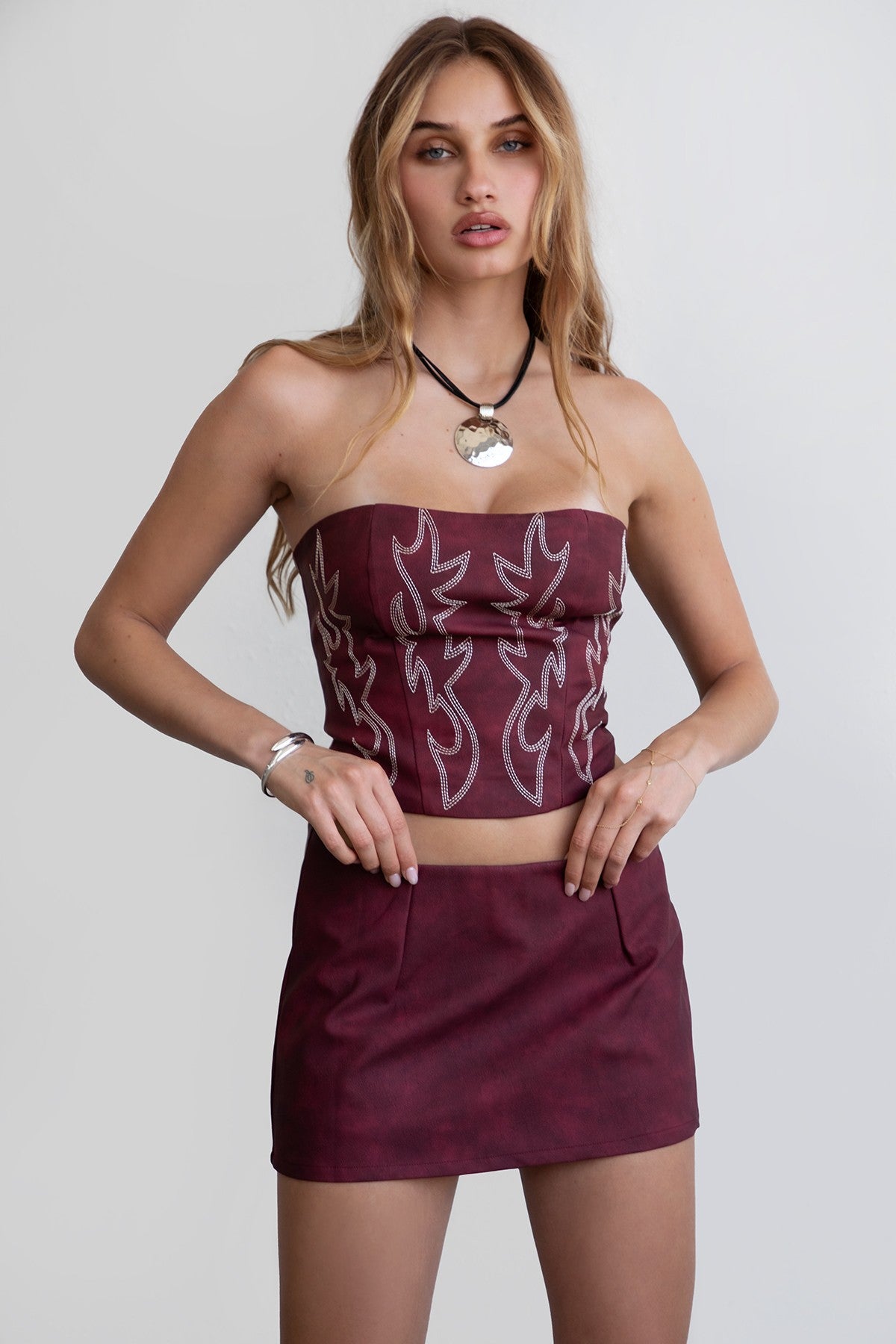 A woman wearing a red strapless corset top with embroidered details and a straight neckline, paired with a mini skirt.