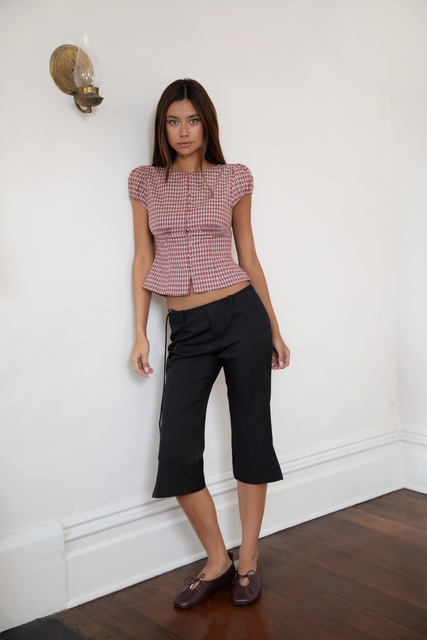 Woman wearing TIC TOC TA32072 DARIS gingham puff sleeve blouse top featuring soft cotton gingham fabric with a classic check pattern, cropped feminine fit, round neckline with front button closure, puff short sleeves, smocked back panel, and under bust smocking for a vintage-inspired western look.