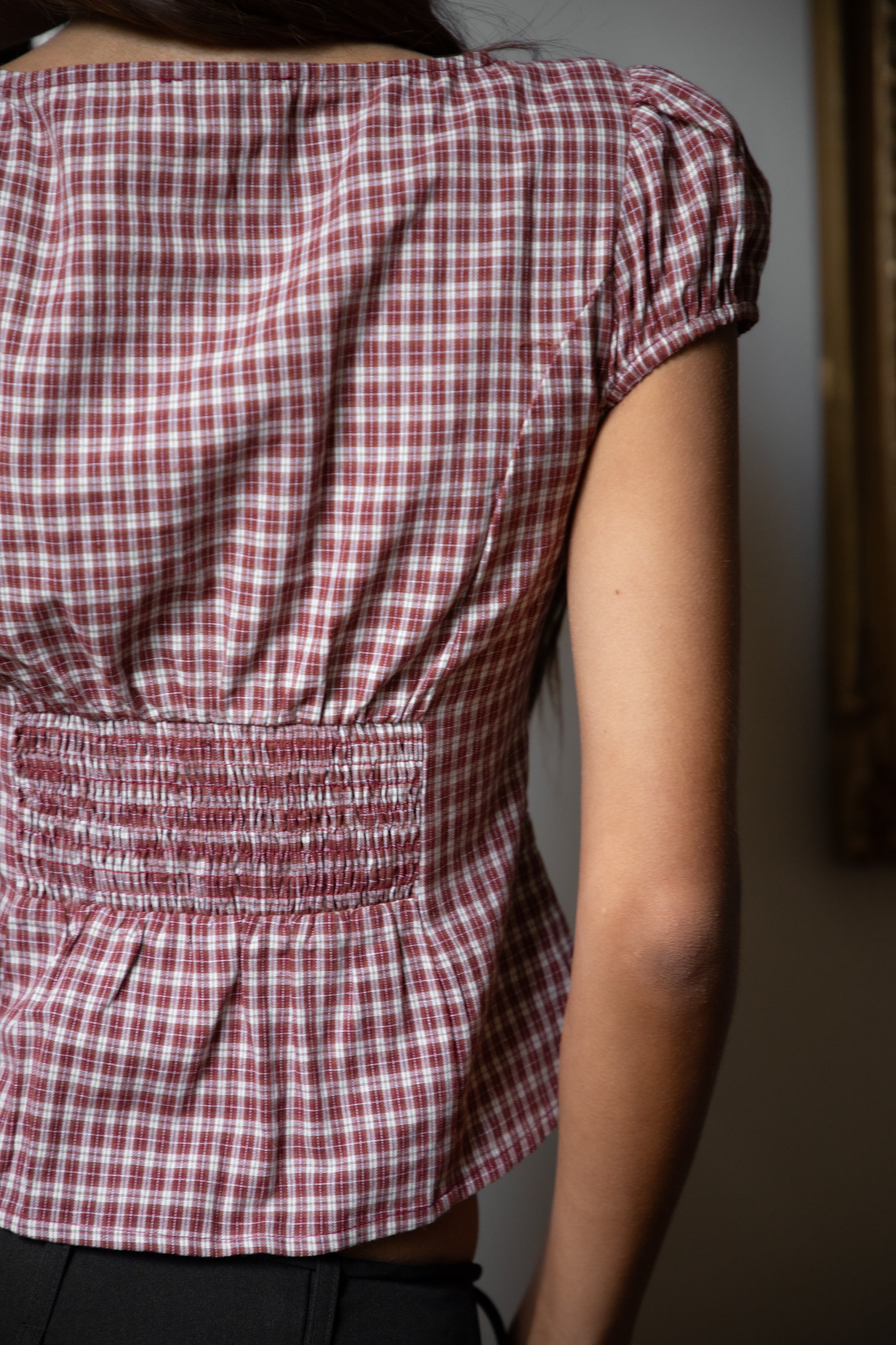 Woman wearing TIC TOC TA32072 DARIS gingham puff sleeve blouse top featuring soft cotton gingham fabric with a classic check pattern, cropped feminine fit, round neckline with front button closure, puff short sleeves, smocked back panel, and under bust smocking for a vintage-inspired western look.