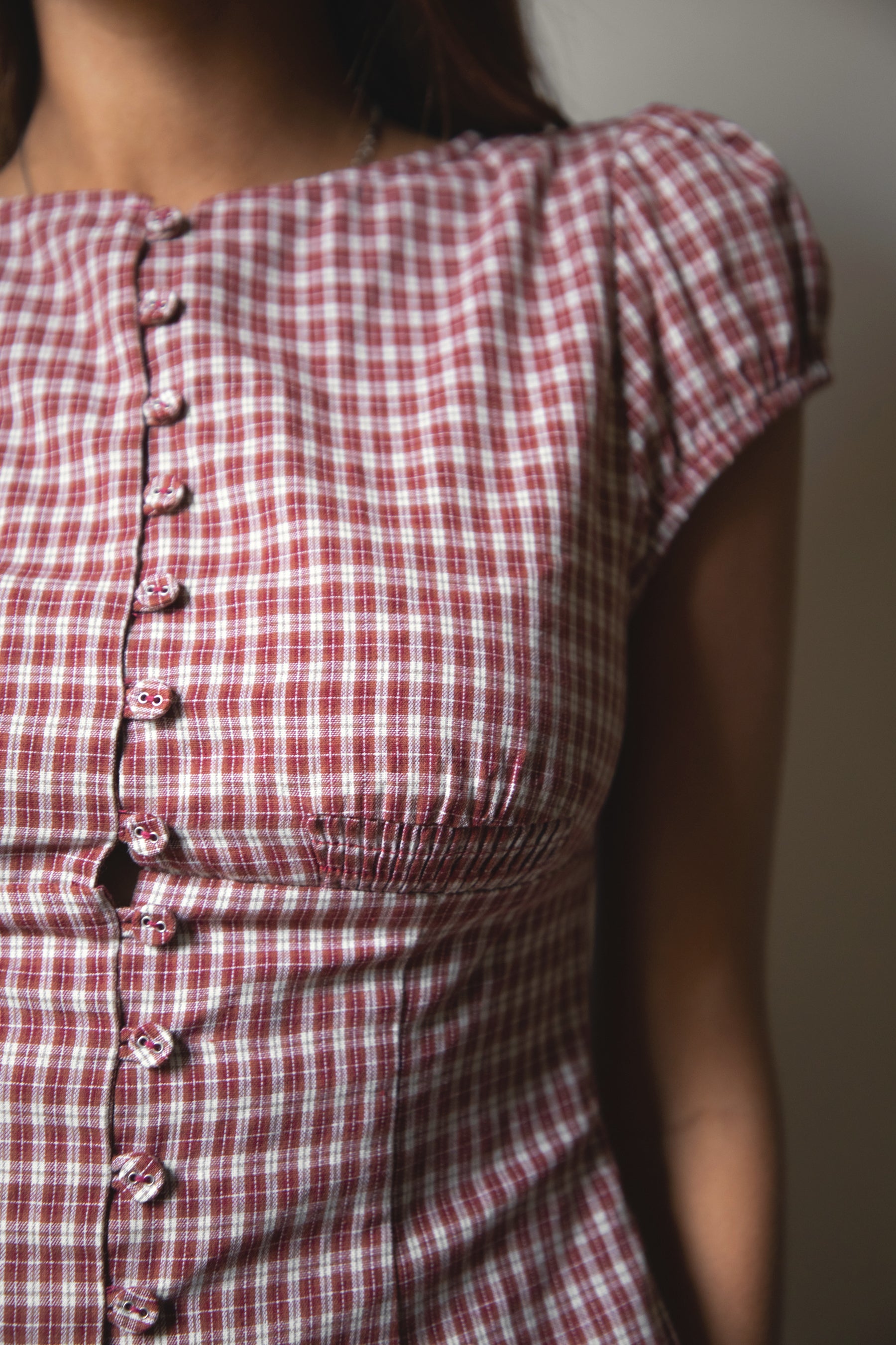 Woman wearing TIC TOC TA32072 DARIS gingham puff sleeve blouse top featuring soft cotton gingham fabric with a classic check pattern, cropped feminine fit, round neckline with front button closure, puff short sleeves, smocked back panel, and under bust smocking for a vintage-inspired western look.