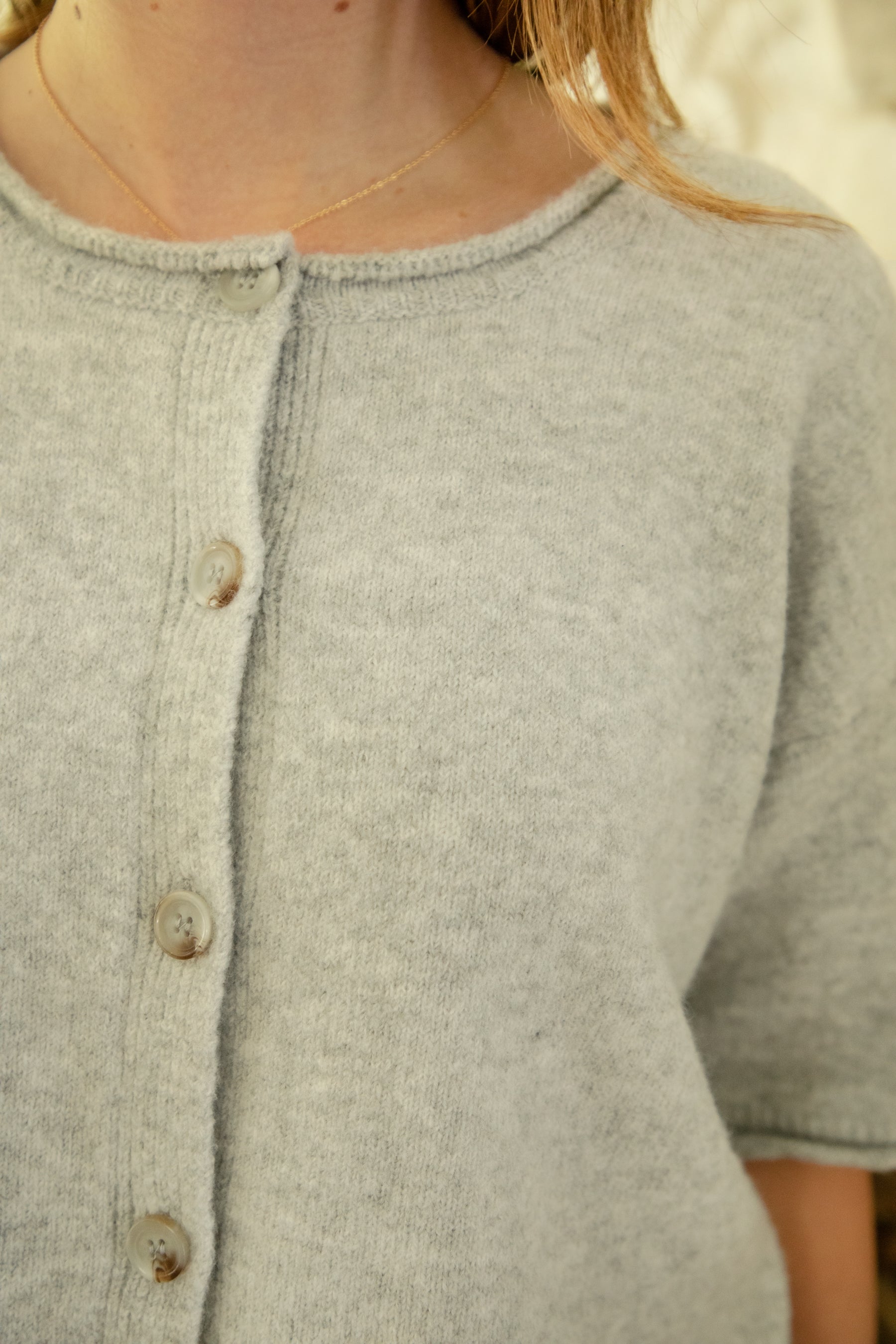Woman wearing HOLLIS roll neck drop shoulder short sleeve knit sweater featuring a minimal rolled neckline, relaxed semi oversized silhouette, short sleeves with rolled cuffs, ribbed hem, front marbled button closure, and lightweight cotton knit for everyday layering.
