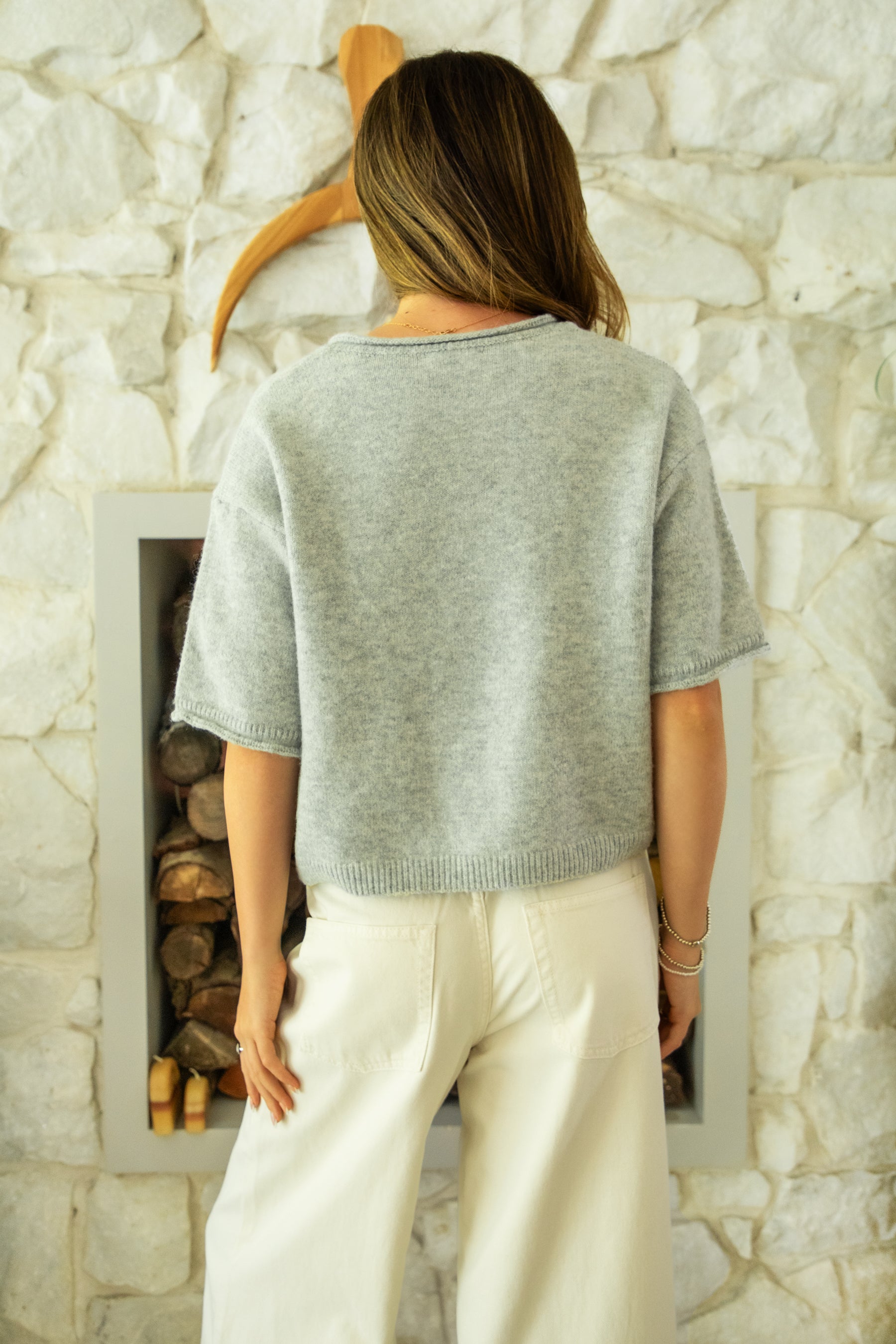 Woman wearing HOLLIS roll neck drop shoulder short sleeve knit sweater featuring a minimal rolled neckline, relaxed semi oversized silhouette, short sleeves with rolled cuffs, ribbed hem, front marbled button closure, and lightweight cotton knit for everyday layering.