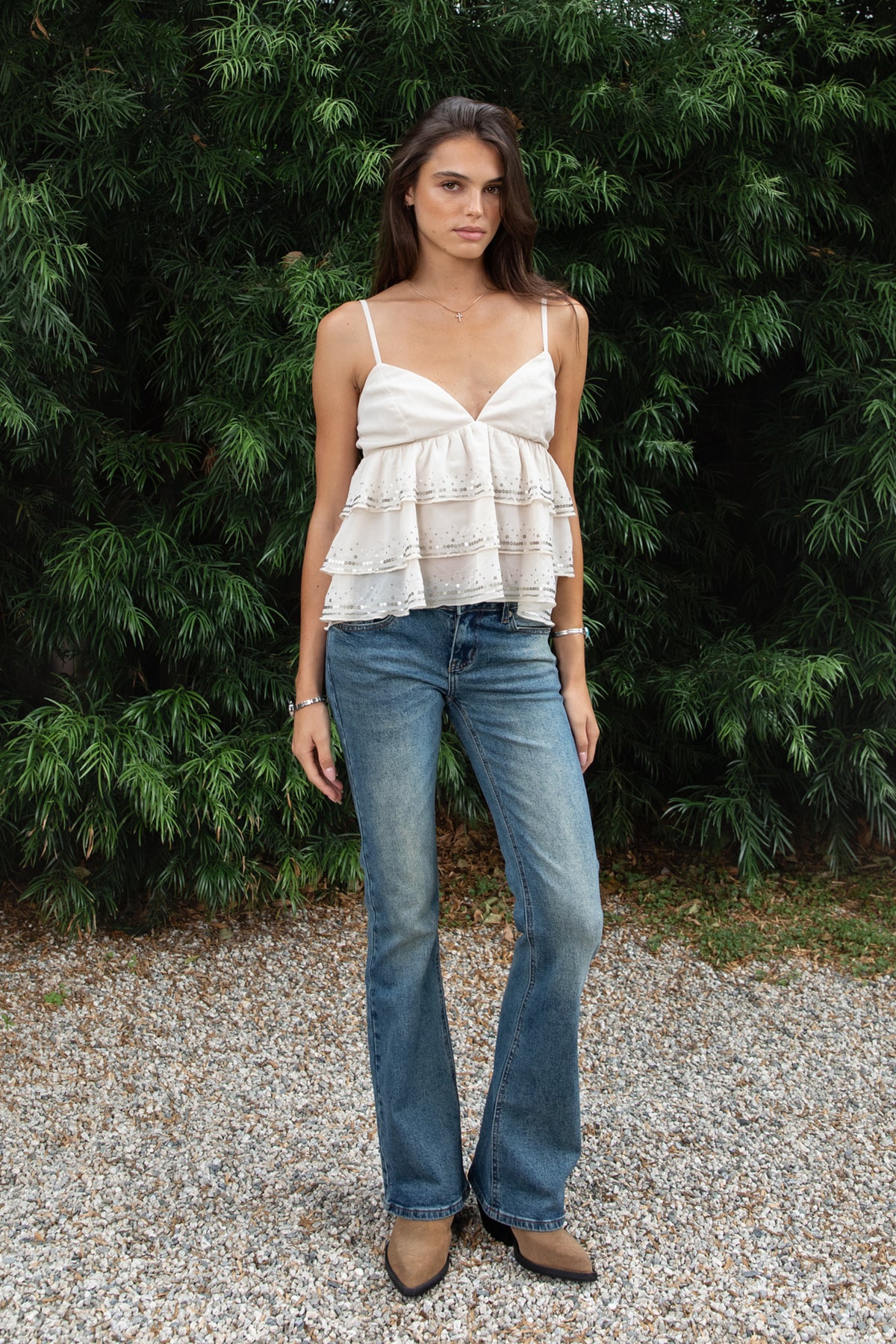 Woman wearing SERAFINA sequin embroidered tiered ruffle cami top featuring lightweight chiffon fabric, deep V neckline with soft triangle bust, adjustable spaghetti shoulder straps, gathered empire waist silhouette, three tiered flowing chiffon ruffles with delicate sequin embroidery, elasticized back, and soft stretch woven lining.