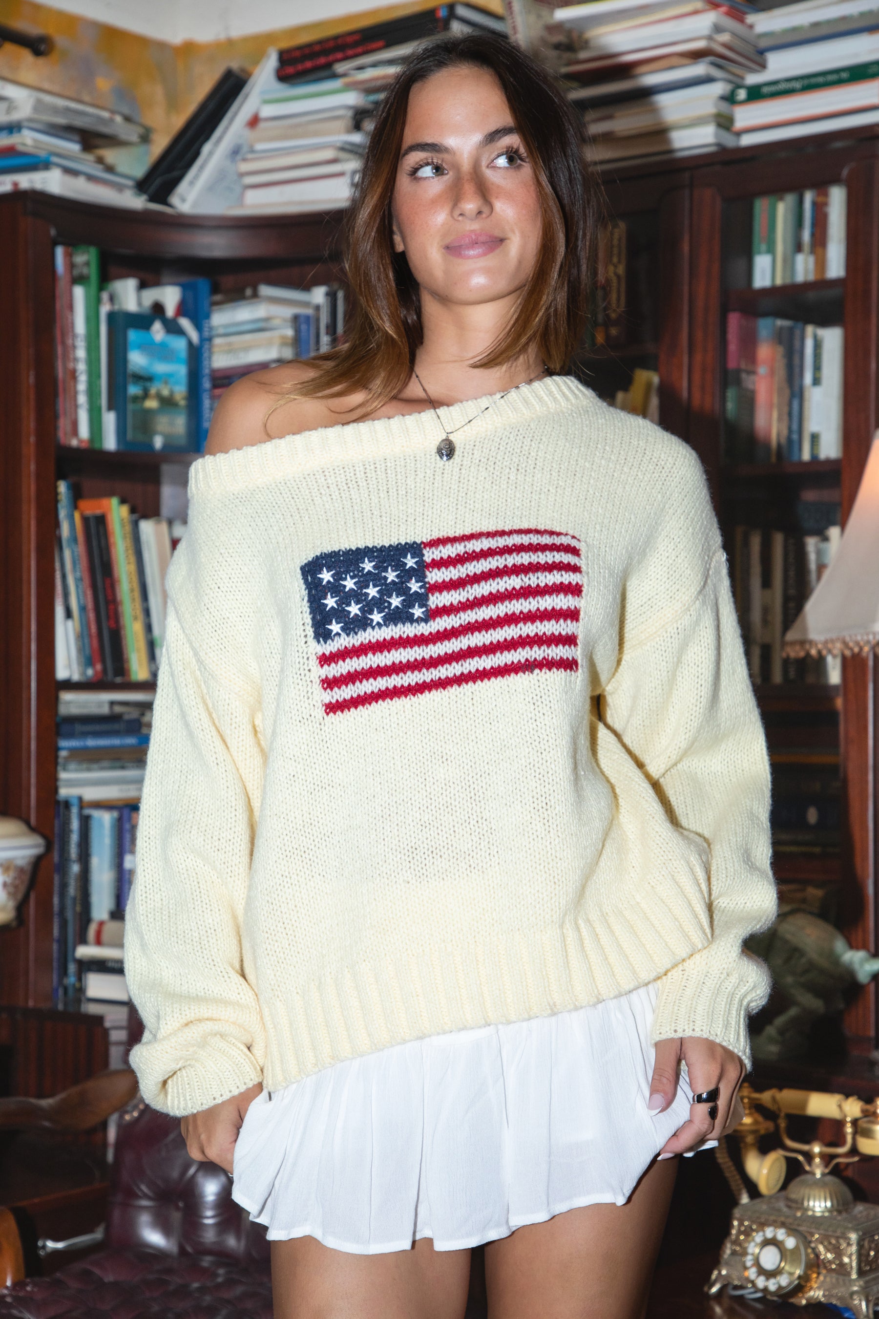 Woman wearing a cream sweater with an American flag design in a room filled with books.