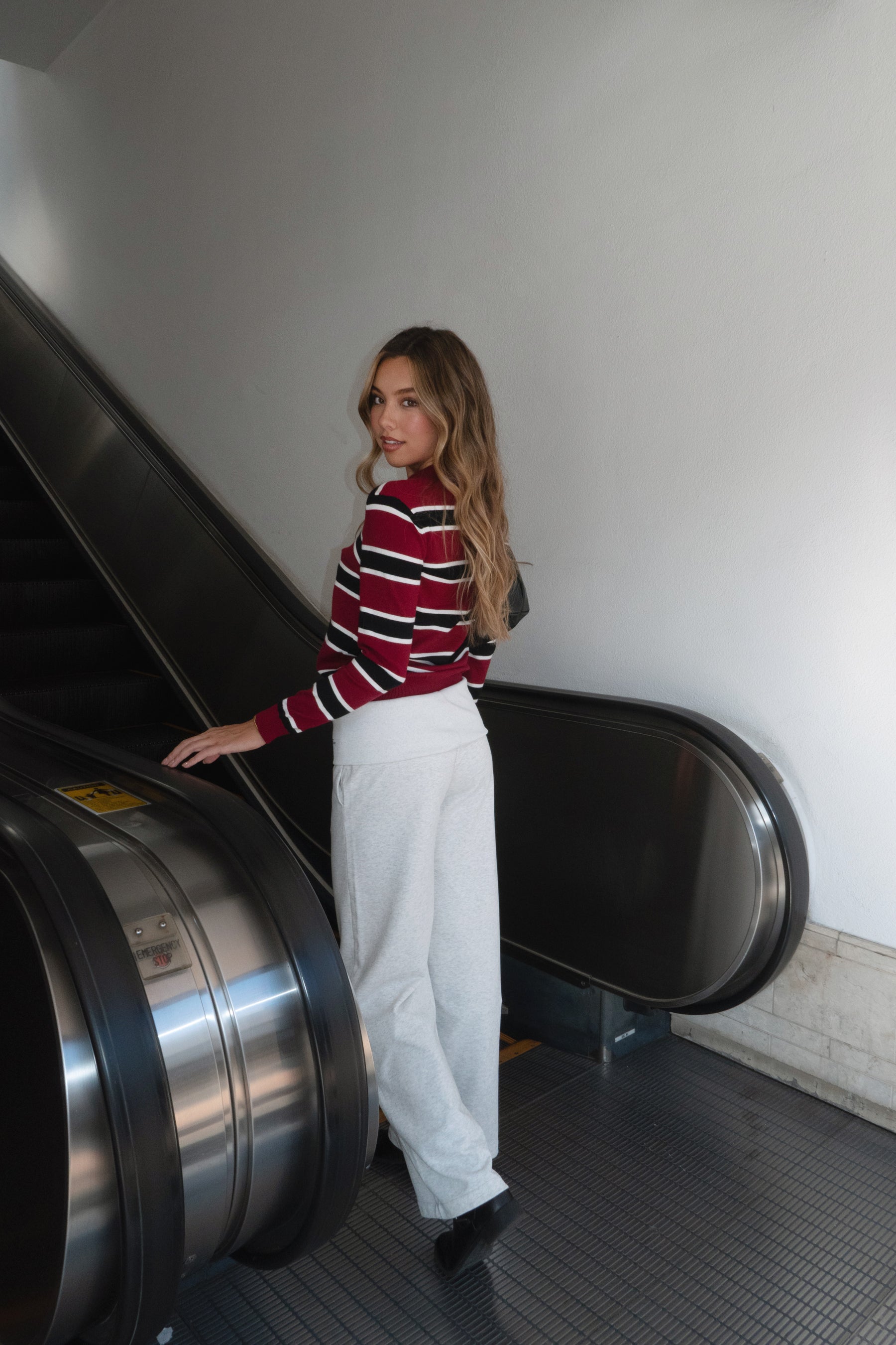 Woman wearing a TIC TOC RHODES Striped Polo T-Shirt red and black striped sweater with white pants, standing indoors.