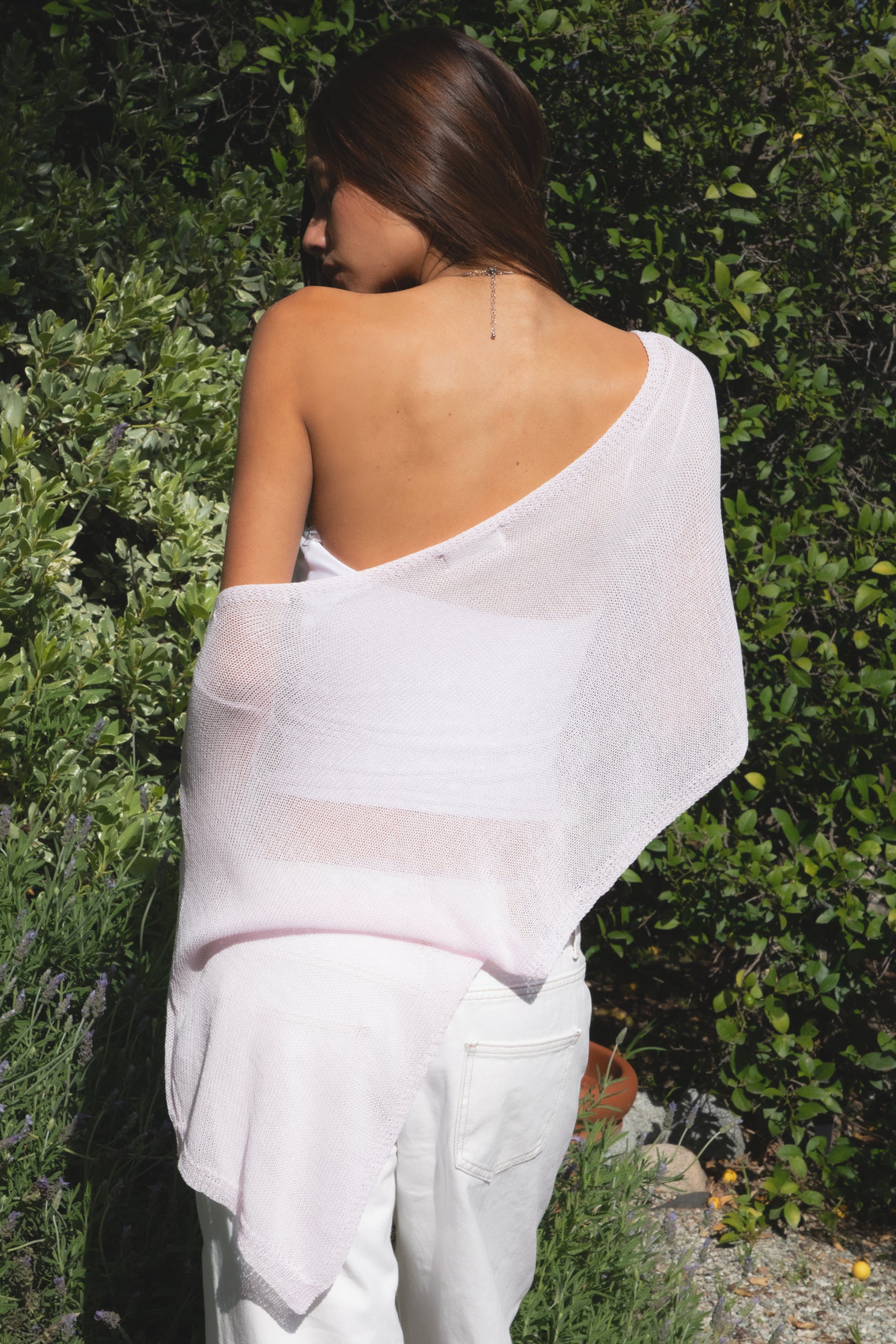 Woman wearing TIC TOC TC31873 SOLEI lightweight open sheer sweater knit poncho in PINK, featuring a wide off-shoulder neckline, airy open knit texture, relaxed draped poncho silhouette, and asymmetrical hem, styled over a white cami with light wash denim for a western-casual summer layering look.