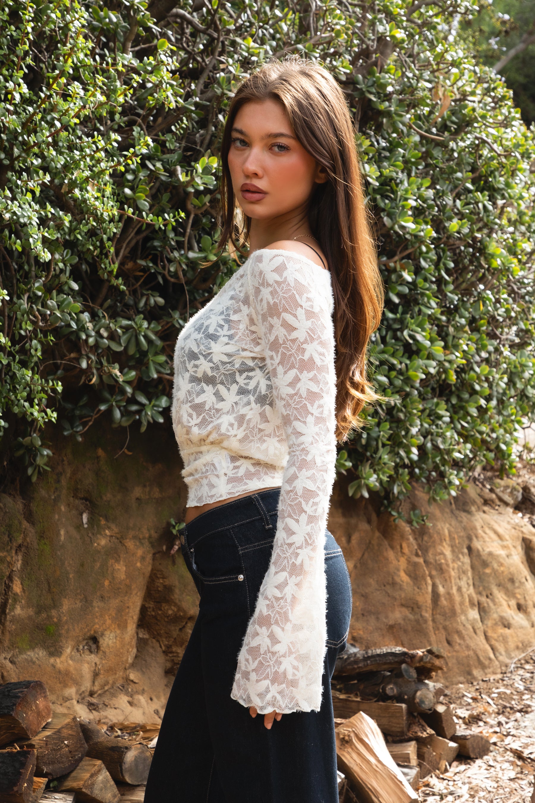Woman wearing TC31934-VELORA floral lace off-shoulder top with bell sleeves and cropped slim fit body, styled with high-rise bottoms for a boho Y2K going-out look.
