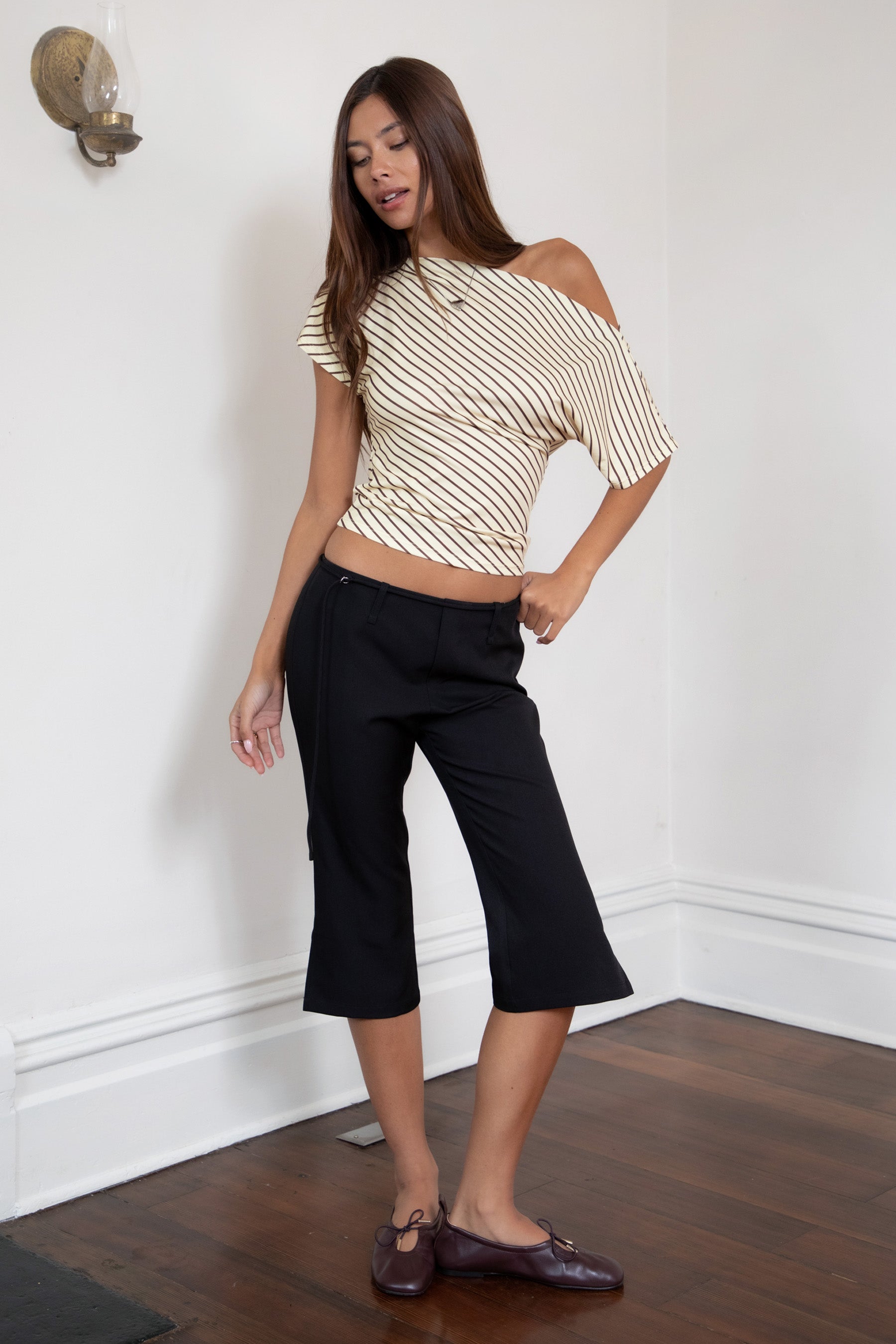 Woman wearing TIC TOC TC32074-AURE AURE striped slash neck ruched waist top featuring soft stretch jersey fabric with a contrast brown pinstripe pattern, wide slash neckline styled off one shoulder, fitted ruched waist detail, short sleeves, and a cropped hem, paired with high-rise denim for a Y2K casual, trendy street look.