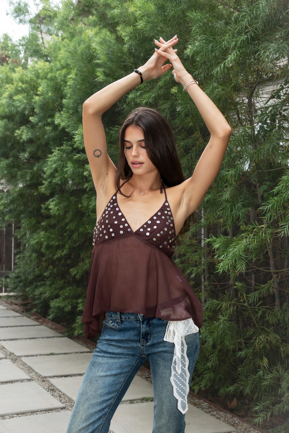 Woman wearing ZAREEN button embellished chiffon halter top featuring flowy yoryu chiffon fabric, feminine sheer finish, deep V neckline, self fabric lined bra cups, iridescent button embellishments across the bust, adjustable self tie halter neckline, smocked back panel, and asymmetric handkerchief hem.
