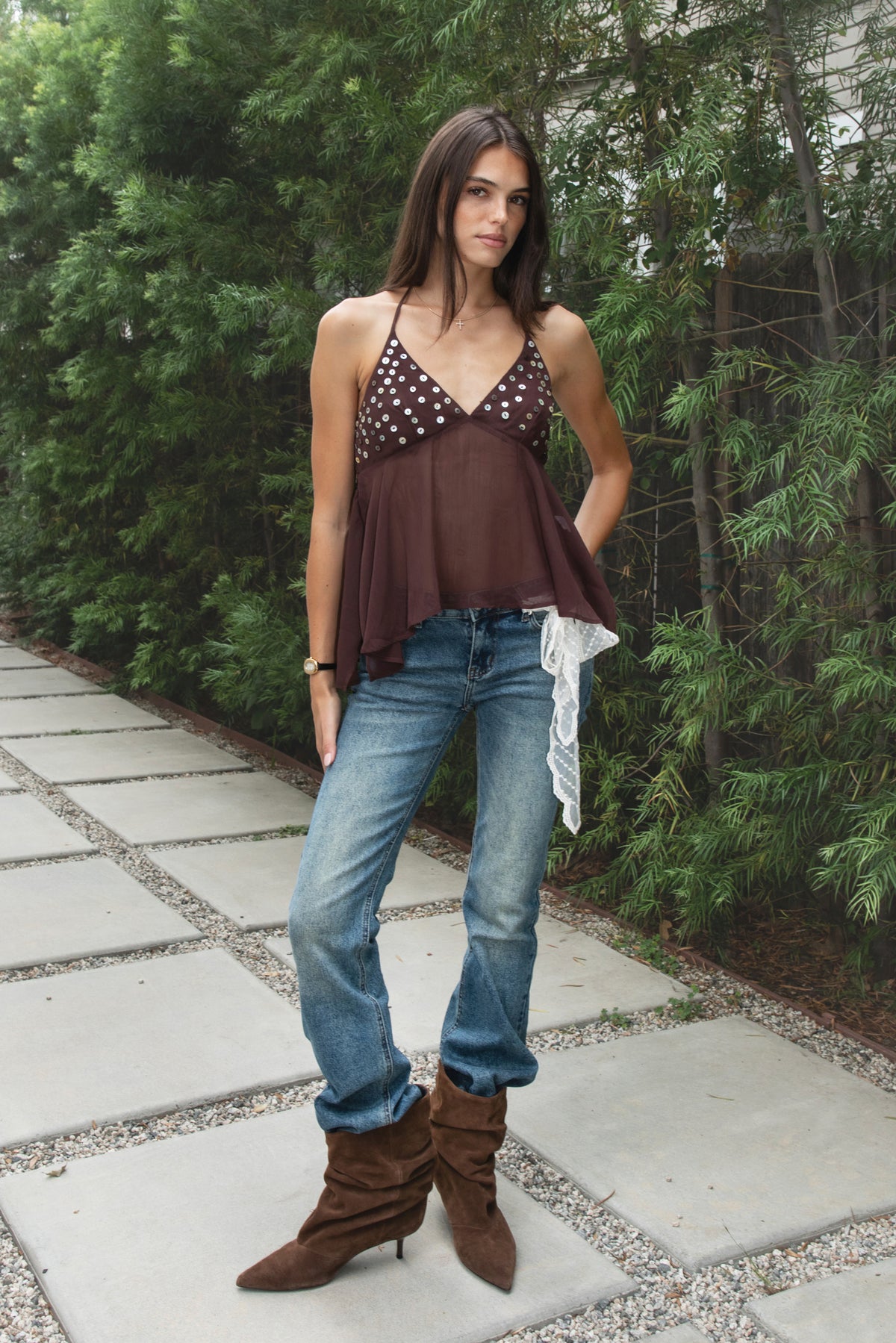 Woman wearing ZAREEN button embellished chiffon halter top featuring flowy yoryu chiffon fabric, feminine sheer finish, deep V neckline, self fabric lined bra cups, iridescent button embellishments across the bust, adjustable self tie halter neckline, smocked back panel, and asymmetric handkerchief hem.