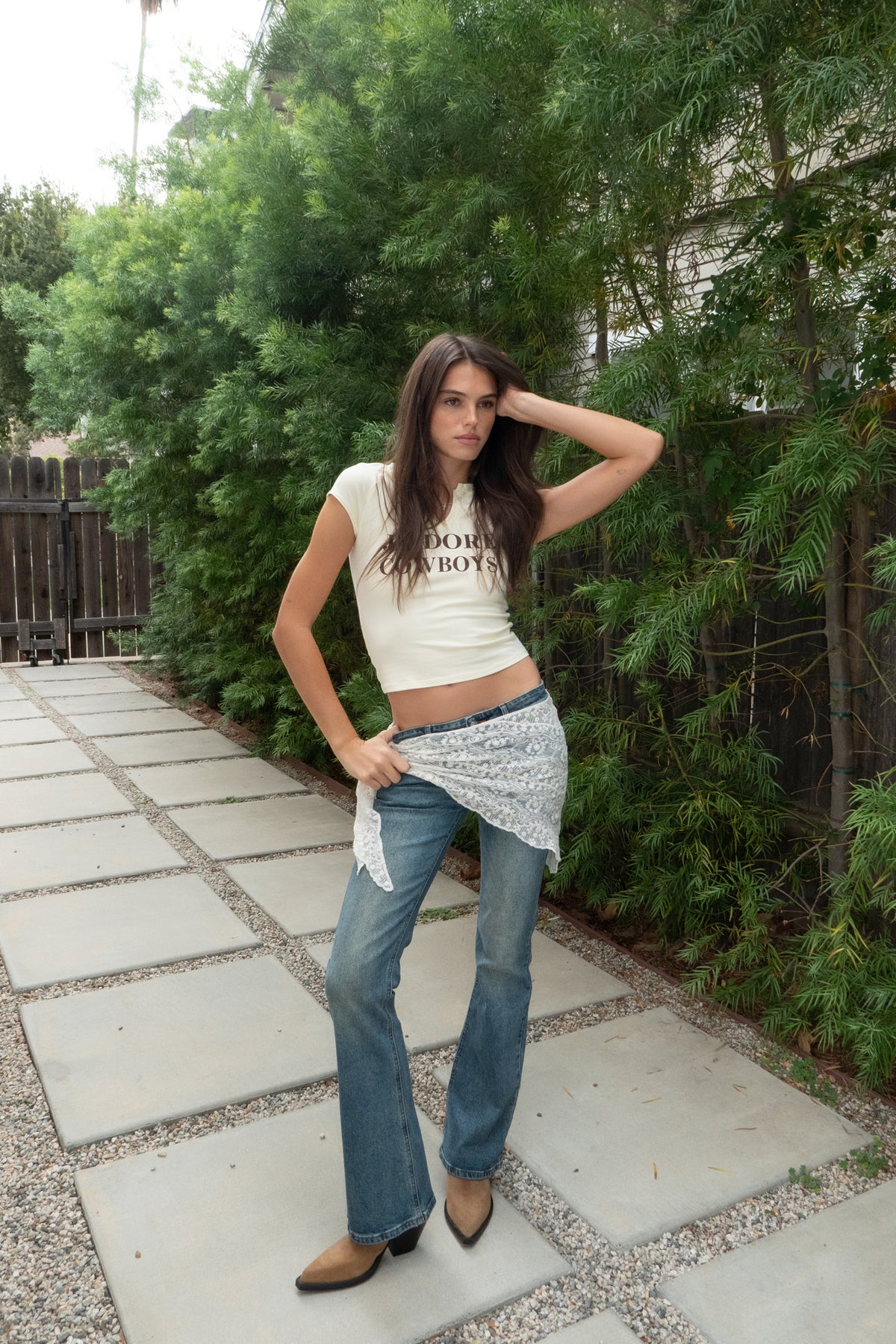Woman wearing J'ADORE Cowboys graphic baby tee featuring soft cotton stretch jersey fabric, J'Adore Cowboys graphic print at the center front, notched V neckline detail, short raglan cap sleeves, slim fitted body silhouette, cropped baby tee length, and smooth lightweight construction for western and casual everyday styling.