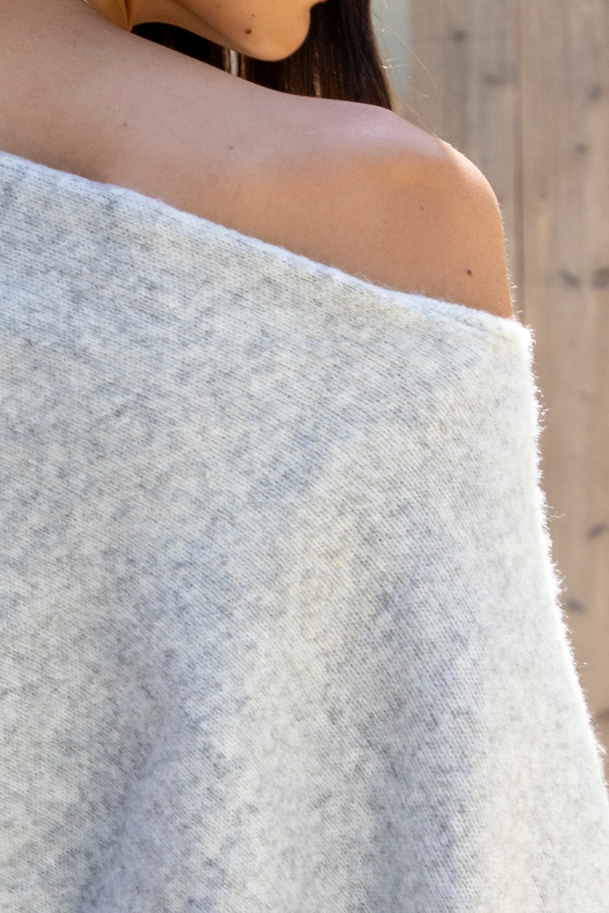 Woman wearing AINSLEY off shoulder asymmetric knit poncho sweater featuring soft brushed sweater knit fabric, cozy warmth, convertible off shoulder neckline, draped poncho silhouette, relaxed asymmetrical design, easy pull on style, and soft stretch comfort for fall and winter layering.