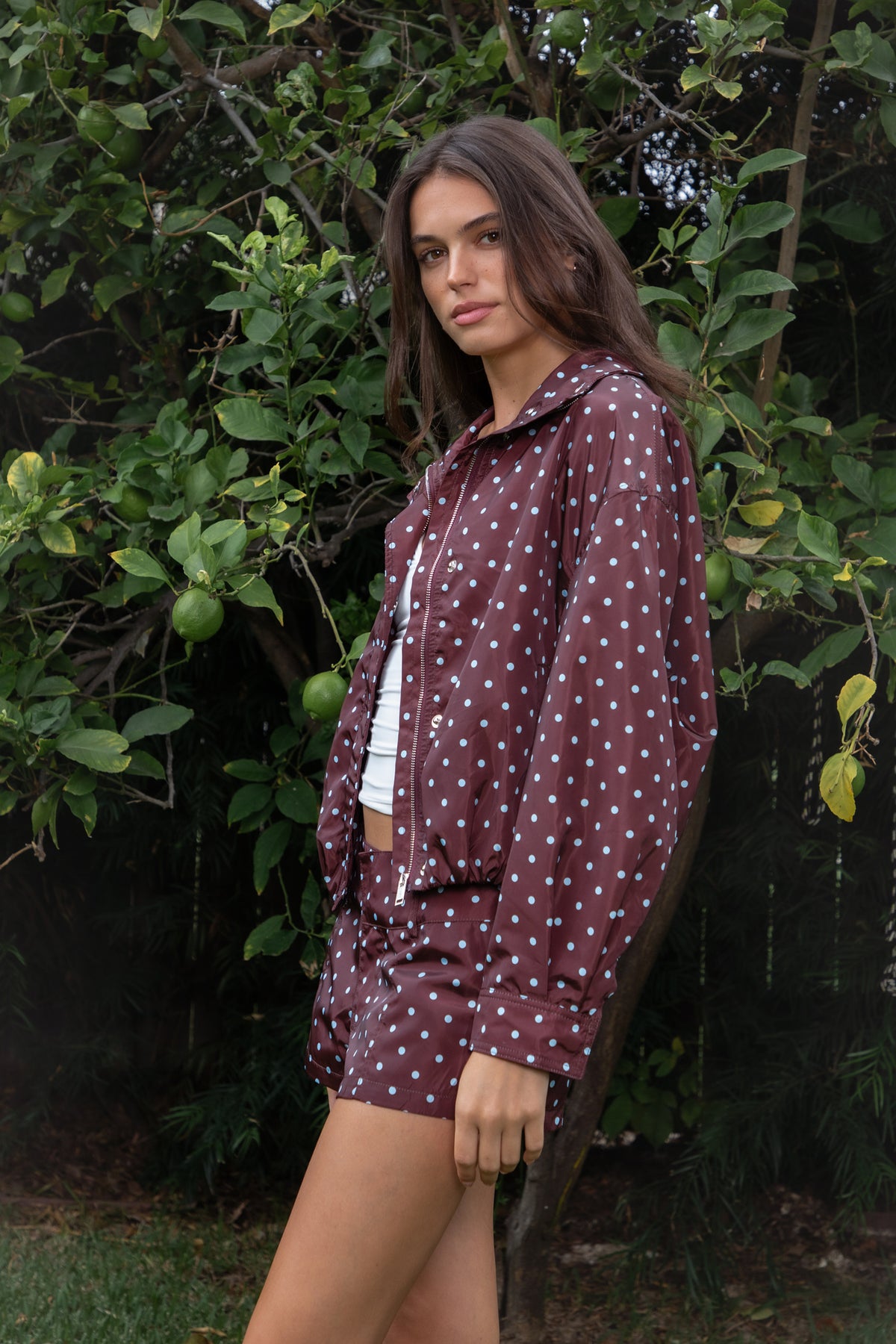 Woman wearing CLEMENTINE embroidered lace up halter mini dress featuring structured stretch fabric, fitted bodycon silhouette, straight neckline with adjustable halter tie straps, floral embroidery with western inspired details, deep center front lace up design with metal eyelets, gold tone stud embellishments along the neckline and hem, corset inspired contoured seaming, exposed back, and short mini length.