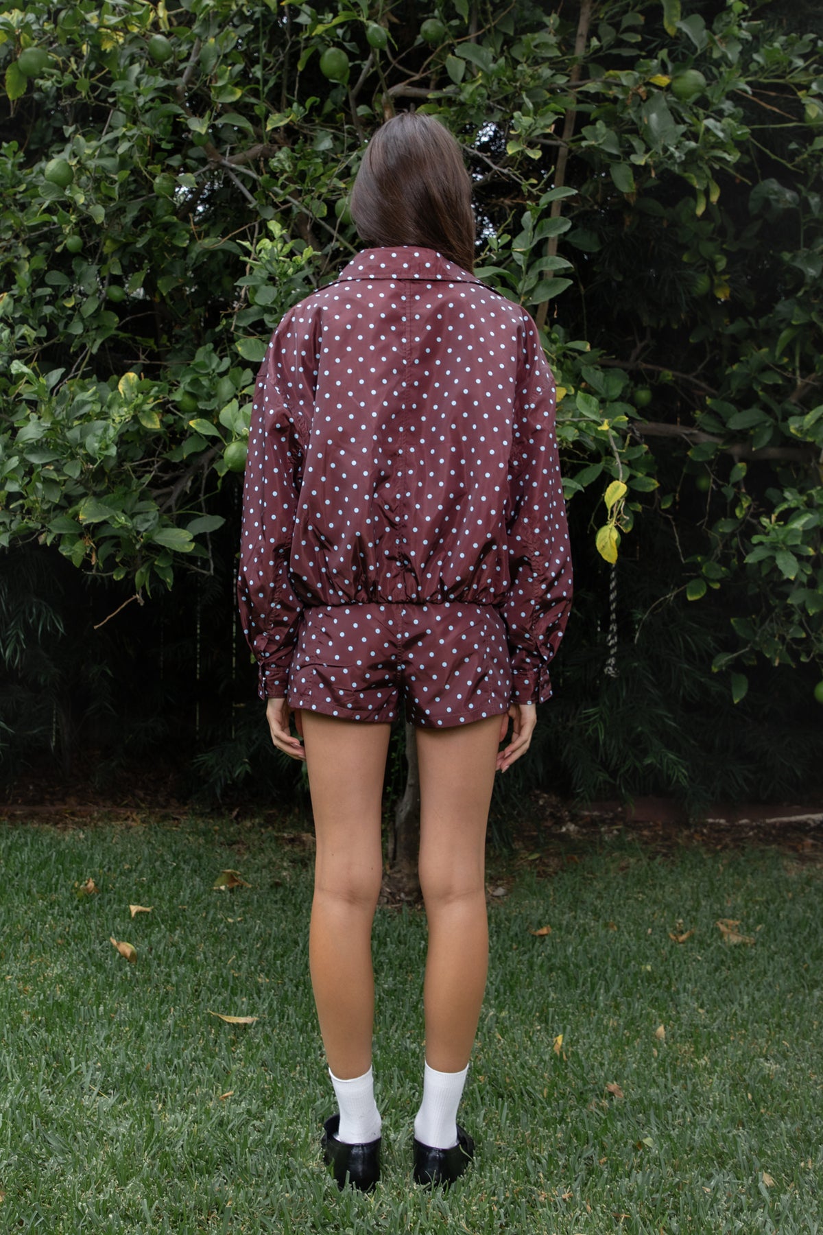 Woman wearing CLEMENTINE embroidered lace up halter mini dress featuring structured stretch fabric, fitted bodycon silhouette, straight neckline with adjustable halter tie straps, floral embroidery with western inspired details, deep center front lace up design with metal eyelets, gold tone stud embellishments along the neckline and hem, corset inspired contoured seaming, exposed back, and short mini length.