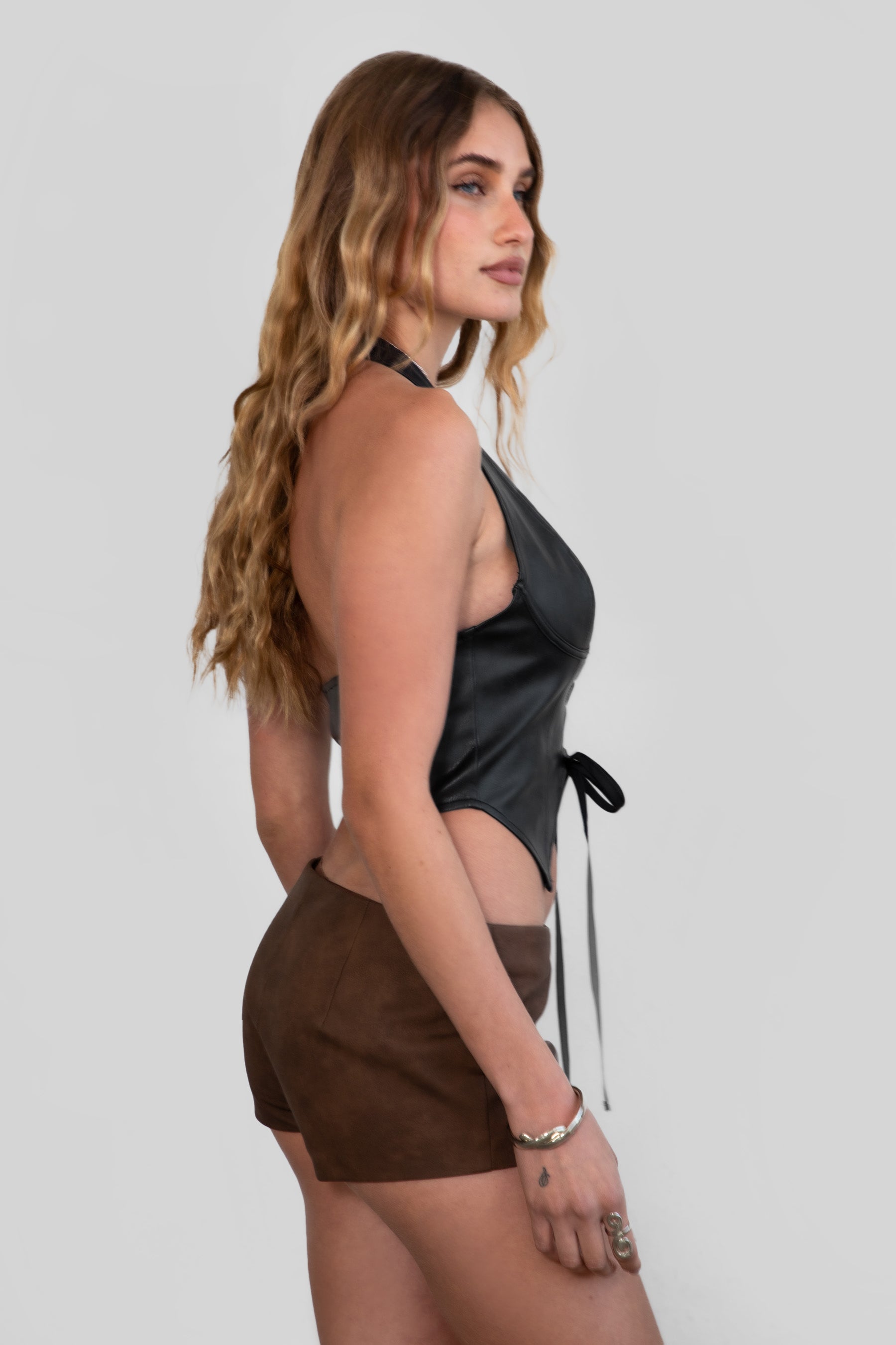 Women wearing TIC TOC CARA Lightweight PU Halter Top in black with deep V neckline, lace detail, and open back design with brown leather shorts.