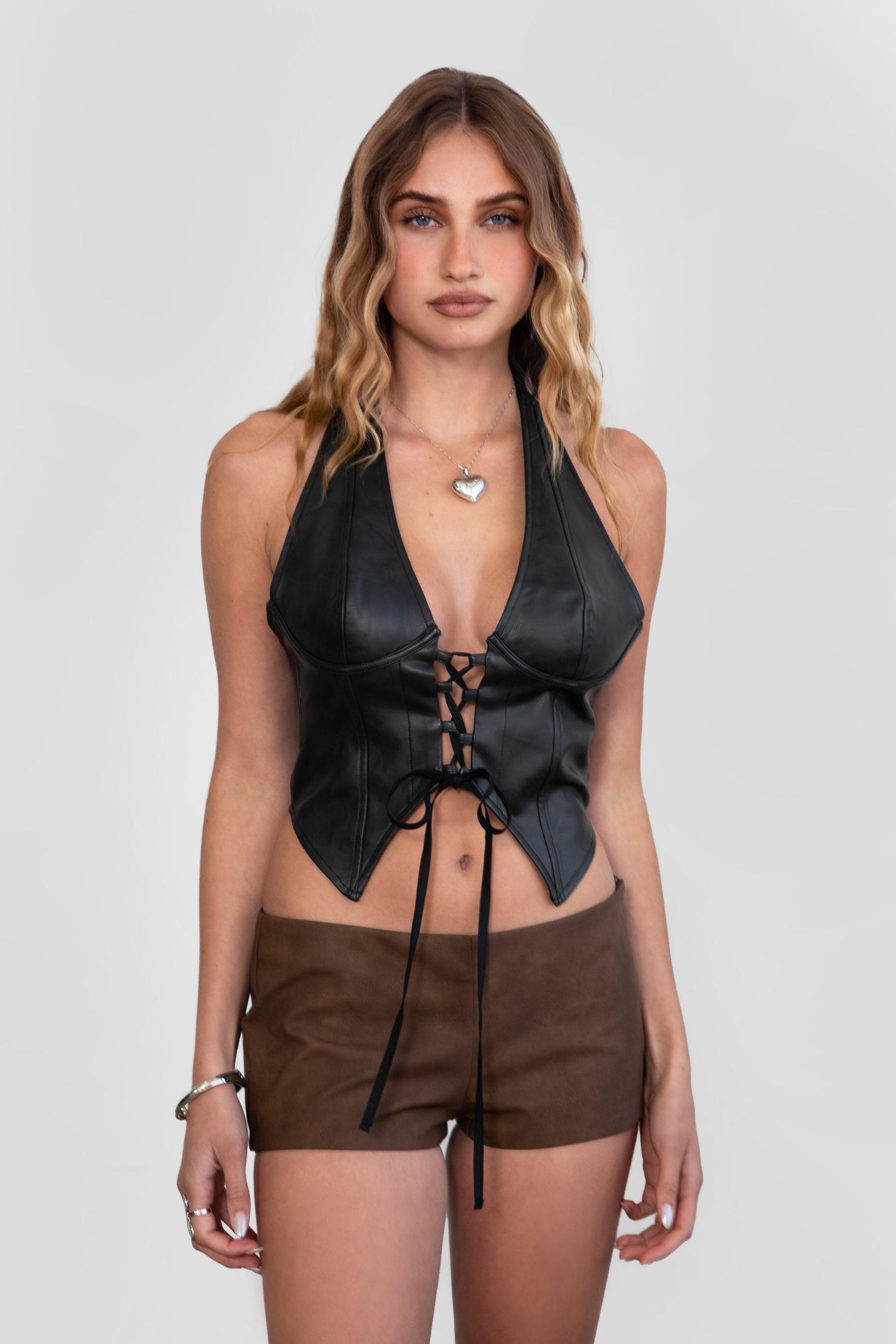 Women wearing TIC TOC CARA Lightweight PU Halter Top in black with deep V neckline, lace detail, and open back design with brown leather shorts.