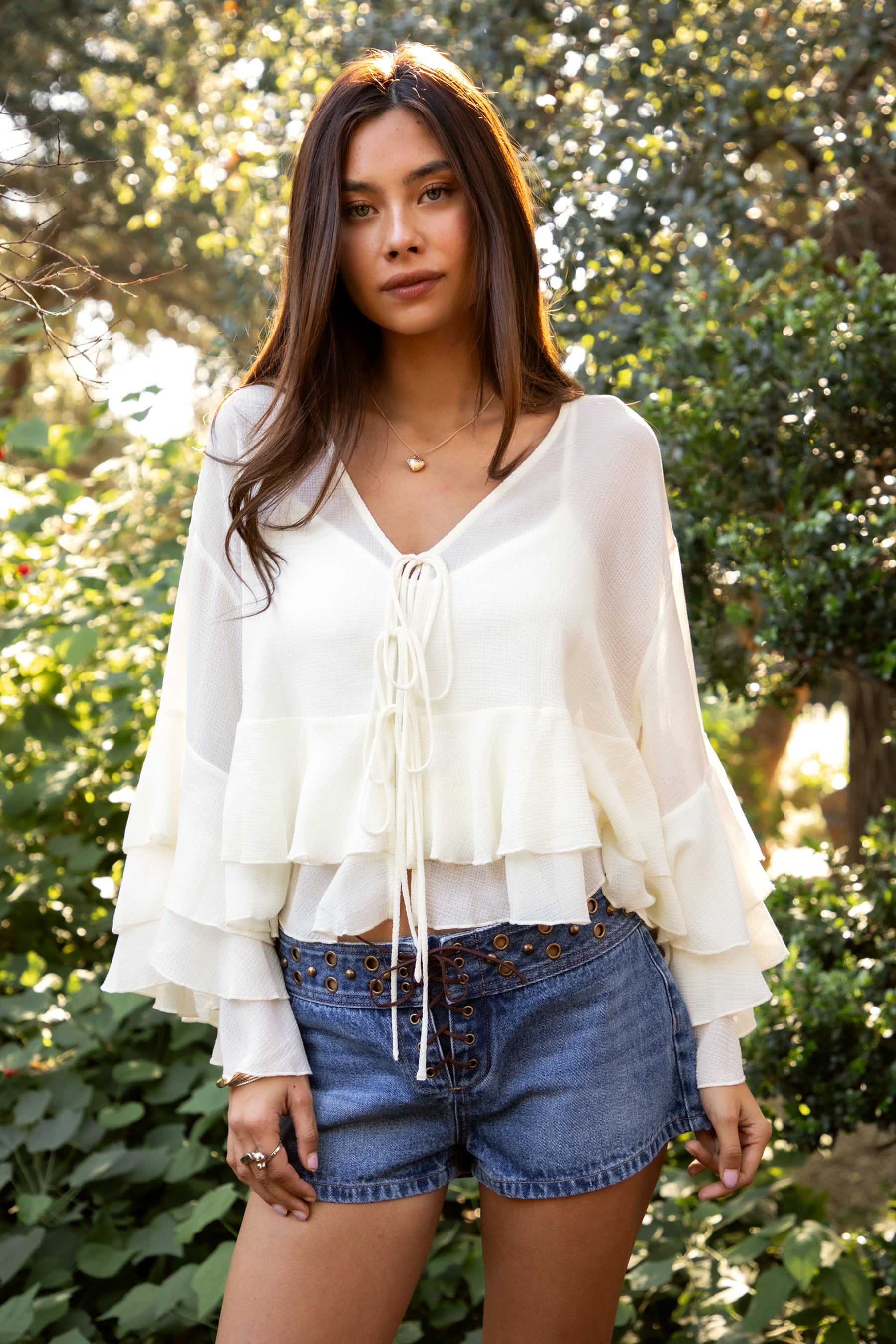 Woman wearing TIC TOC TH31917 BRIEANNE sheer chiffon tiered ruffle blouse featuring a front tie V-neckline, lightweight unlined chiffon body, drop shoulder relaxed fit, and layered ruffle cuffs with a flowy tiered hem, styled for a feminine vacation-ready western look.