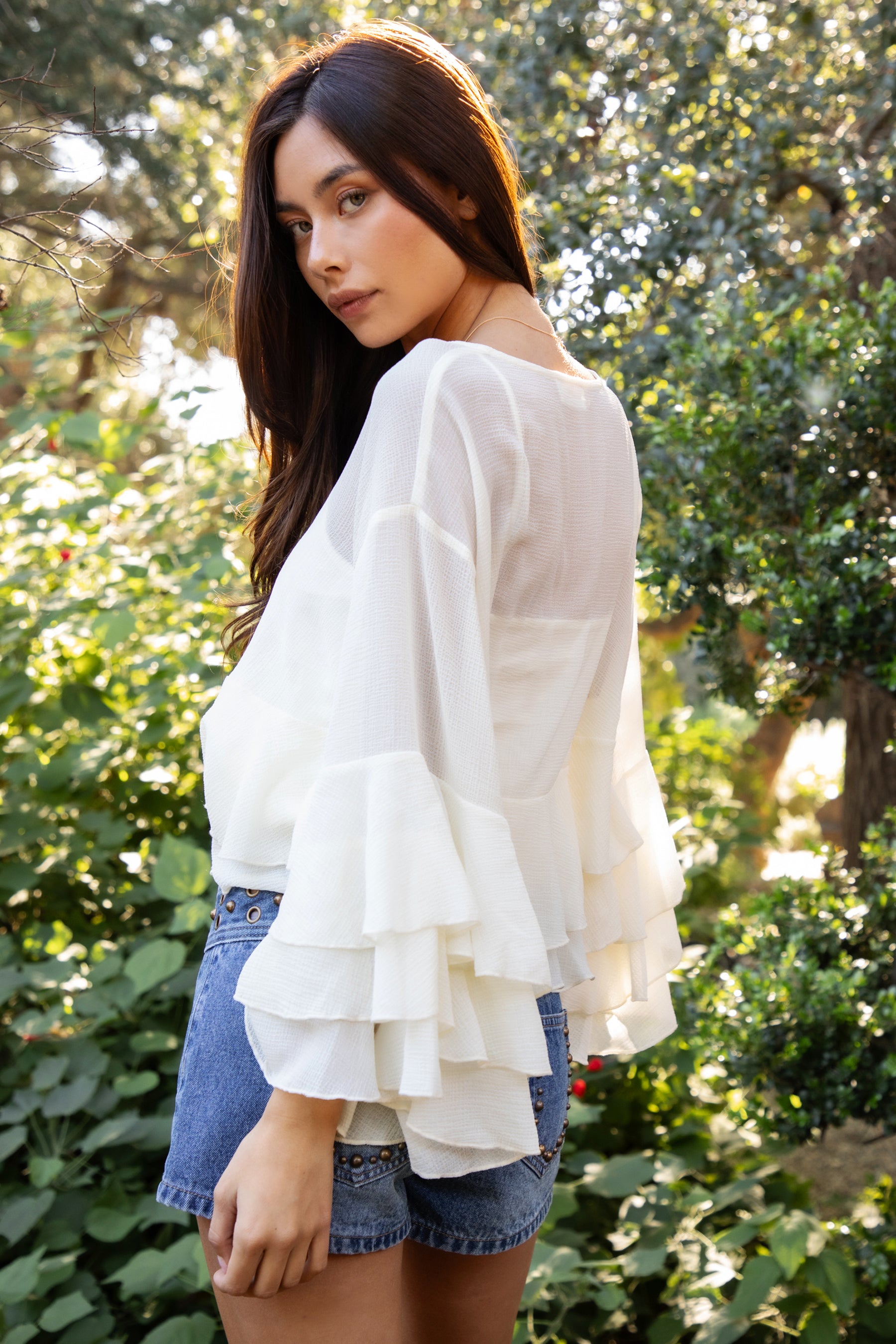 Woman wearing TIC TOC TH31917 BRIEANNE sheer chiffon tiered ruffle blouse featuring a front tie V-neckline, lightweight unlined chiffon body, drop shoulder relaxed fit, and layered ruffle cuffs with a flowy tiered hem, styled for a feminine vacation-ready western look.