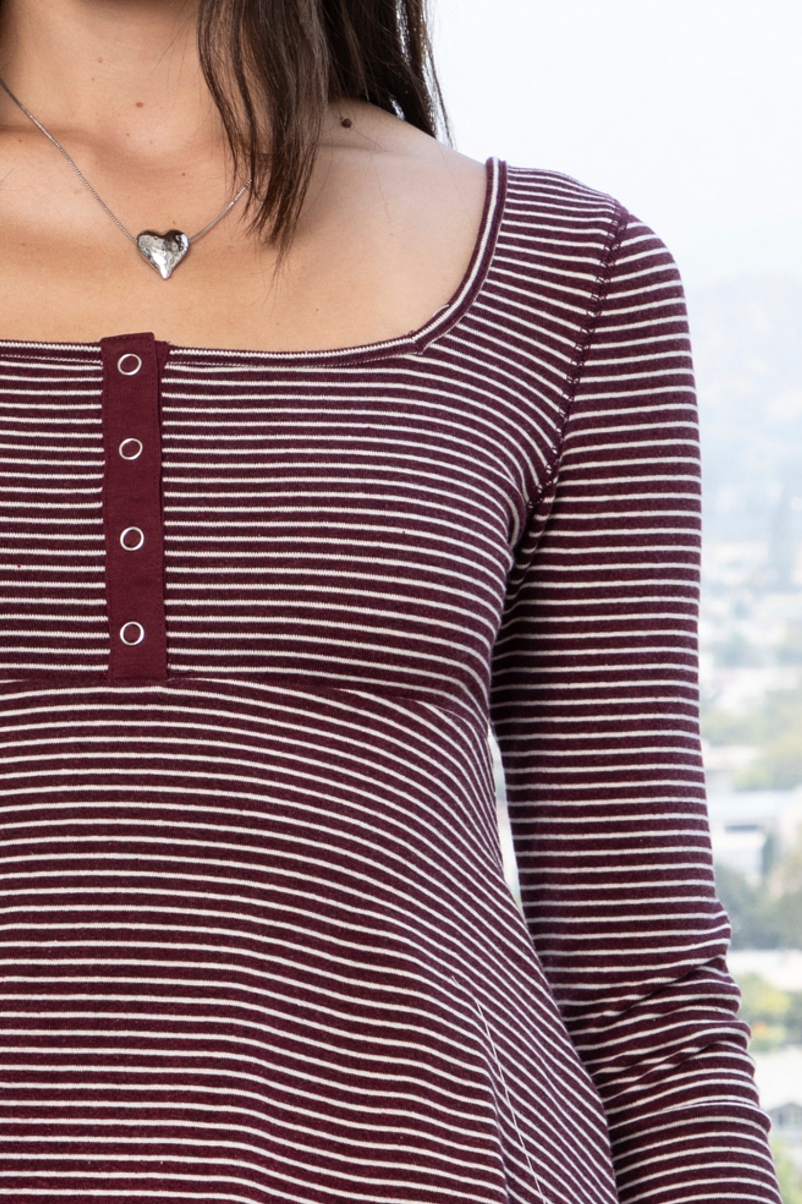Woman wearing ELODY striped babydoll square neck henley peplum top featuring soft striped knit fabric, wide scoop neckline with contrast trim, henley inspired front placket with metal snap details, fitted bodice, empire waist seam, flared peplum hem, and long fitted sleeves.
