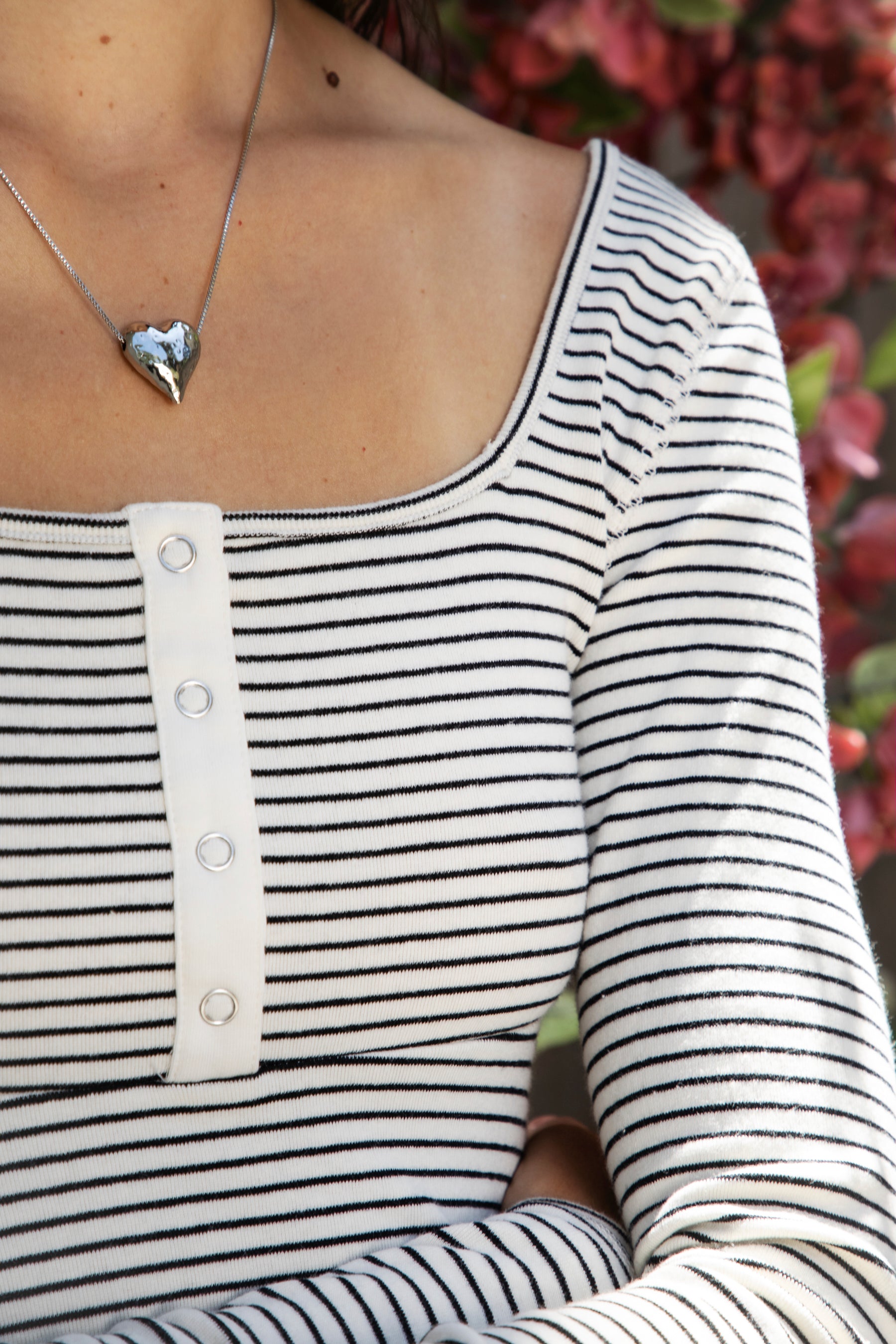 Woman wearing ELODY striped babydoll square neck henley peplum top featuring soft striped knit fabric, wide scoop neckline with contrast trim, henley inspired front placket with metal snap details, fitted bodice, empire waist seam, flared peplum hem, and long fitted sleeves.