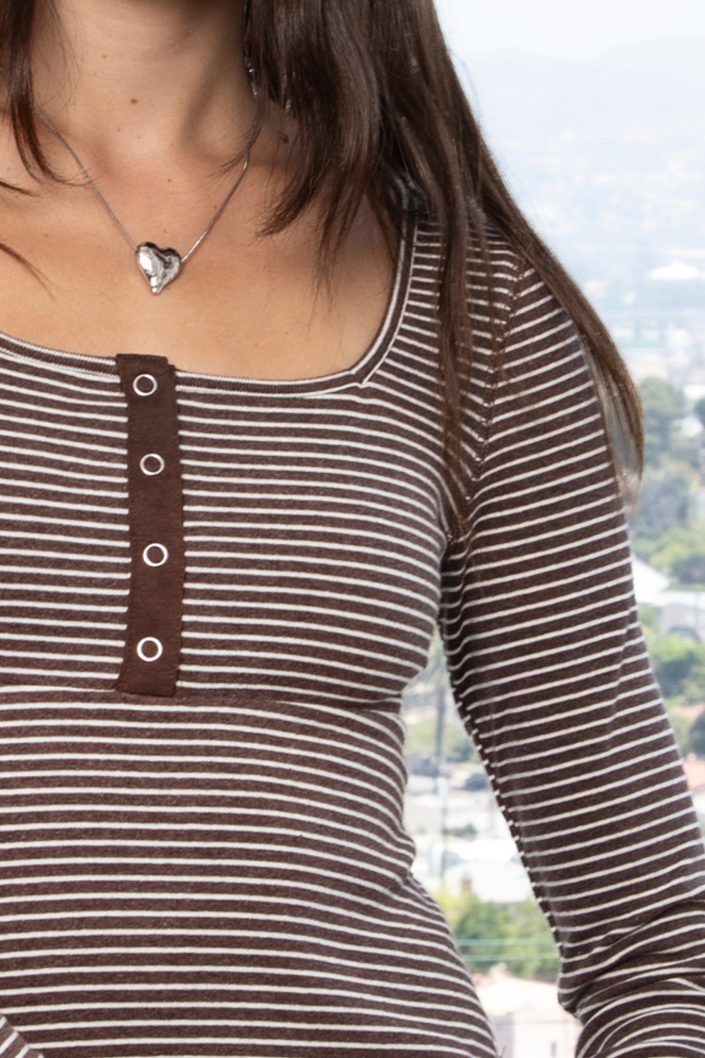Woman wearing ELODY striped babydoll square neck henley peplum top featuring soft striped knit fabric, wide scoop neckline with contrast trim, henley inspired front placket with metal snap details, fitted bodice, empire waist seam, flared peplum hem, and long fitted sleeves.