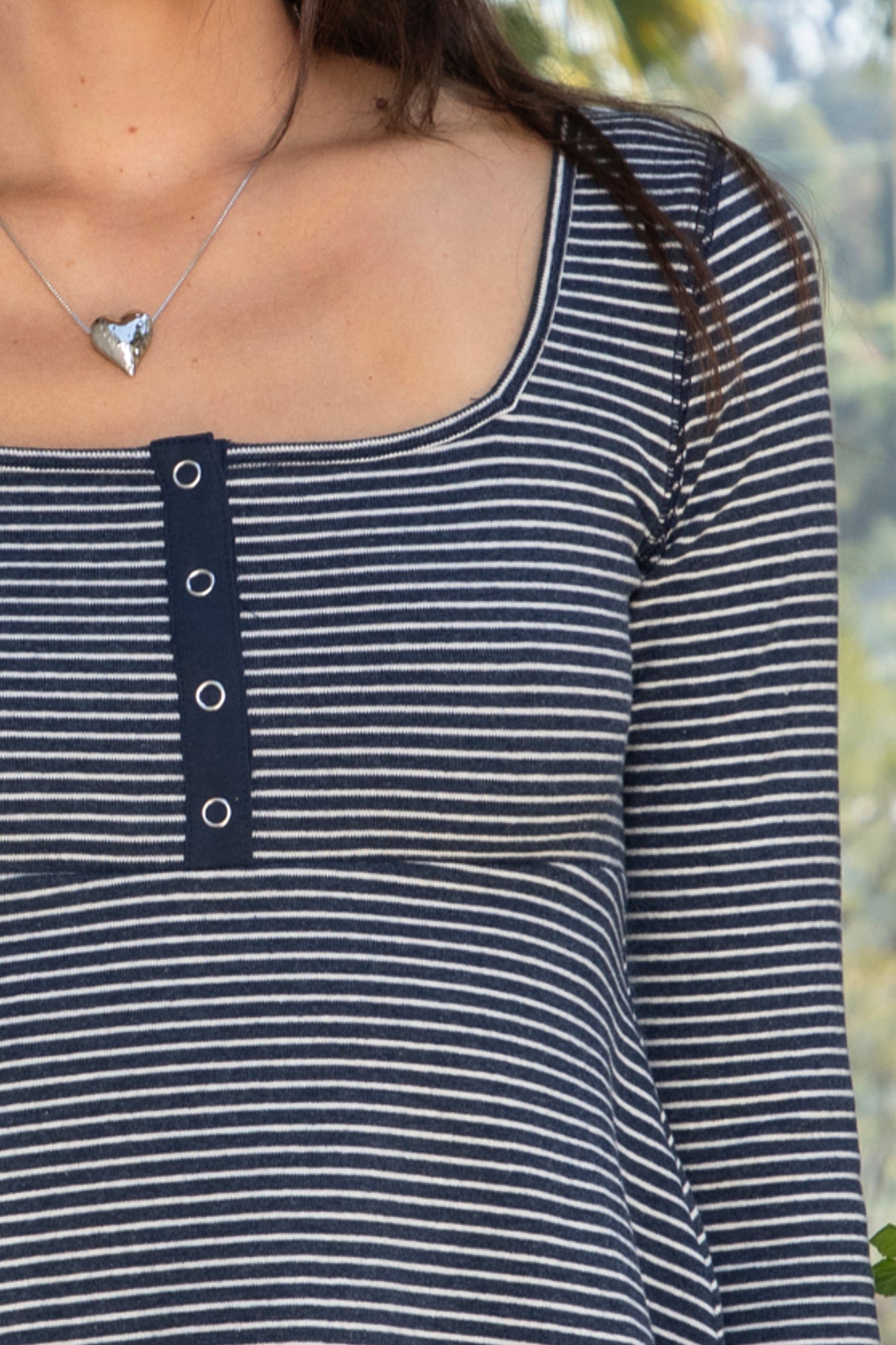 Woman wearing ELODY striped babydoll square neck henley peplum top featuring soft striped knit fabric, wide scoop neckline with contrast trim, henley inspired front placket with metal snap details, fitted bodice, empire waist seam, flared peplum hem, and long fitted sleeves.