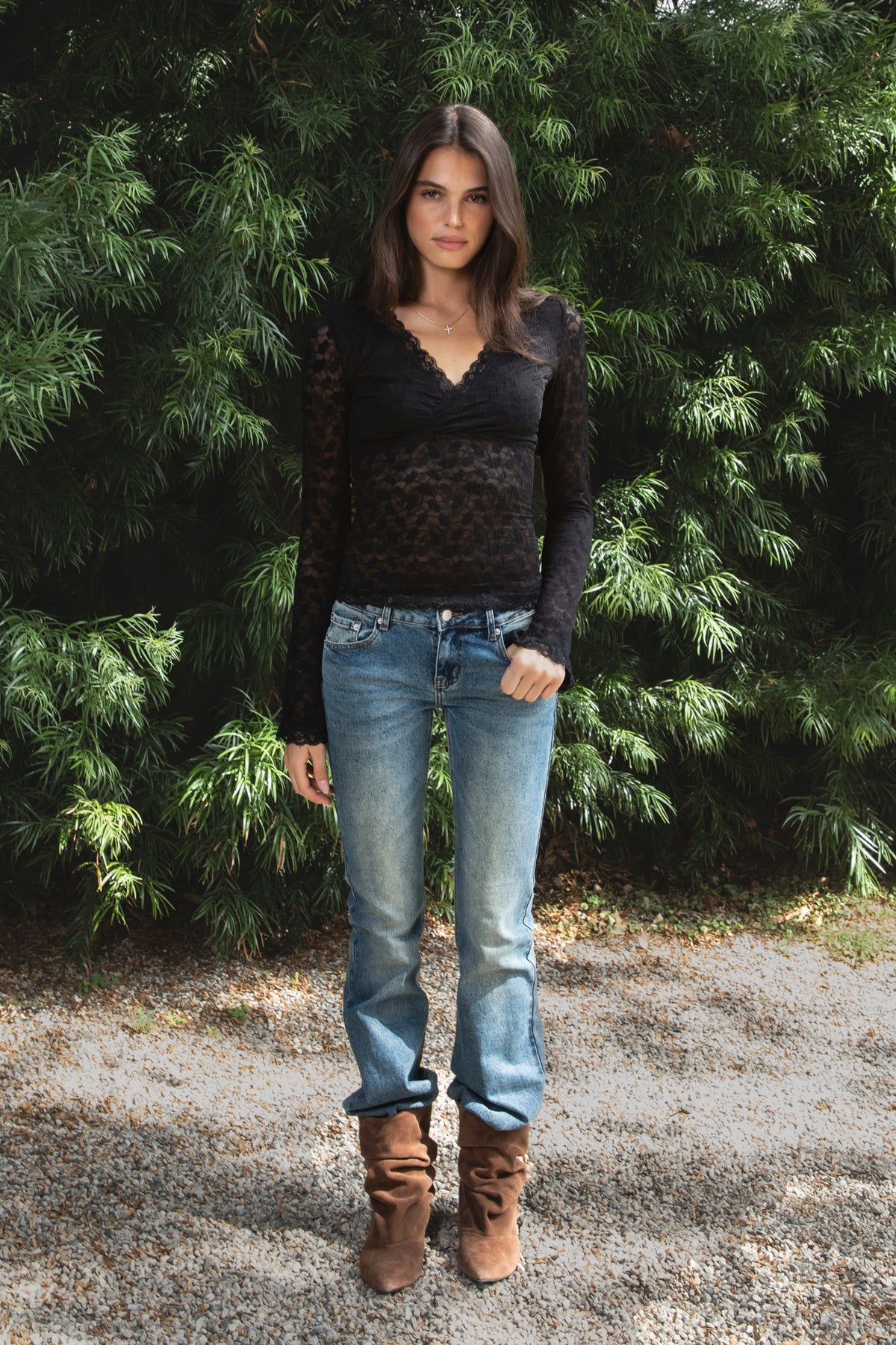 Woman wearing EMMELINE ruched lace long sleeve top featuring sheer floral stretch lace, fitted feminine silhouette, deep V neckline with scalloped lace trim, ruched detailing through the front and sides, soft mesh bust lining, sheer fitted long sleeves, flared lace trimmed cuffs, and scalloped hem finish.