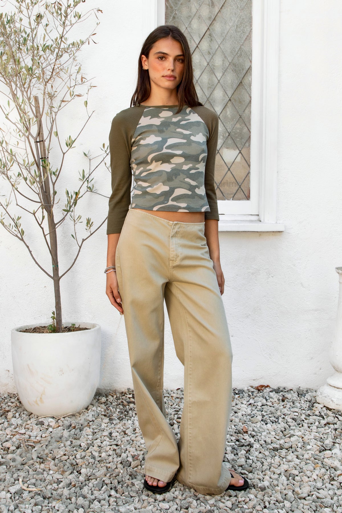 Woman wearing MARCEAU camo waffle raglan top featuring soft waffle jersey fabric, allover camo print body, contrast solid sleeves, classic crew neckline, raglan sleeve construction, three quarter length sleeves, fitted everyday silhouette, and cropped length that sits naturally at the waist.