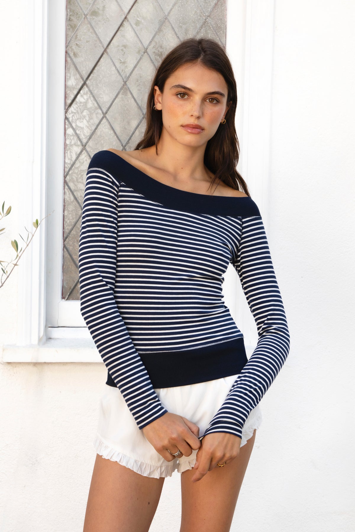 Woman wearing ALIZEE contrast striped off shoulder long sleeve top featuring classic striped jersey fabric, wide solid rib neckline, fitted feminine silhouette, long fitted sleeves, contrast solid rib hem band, hip length fit, and soft stretch construction for casual everyday and transitional styling.