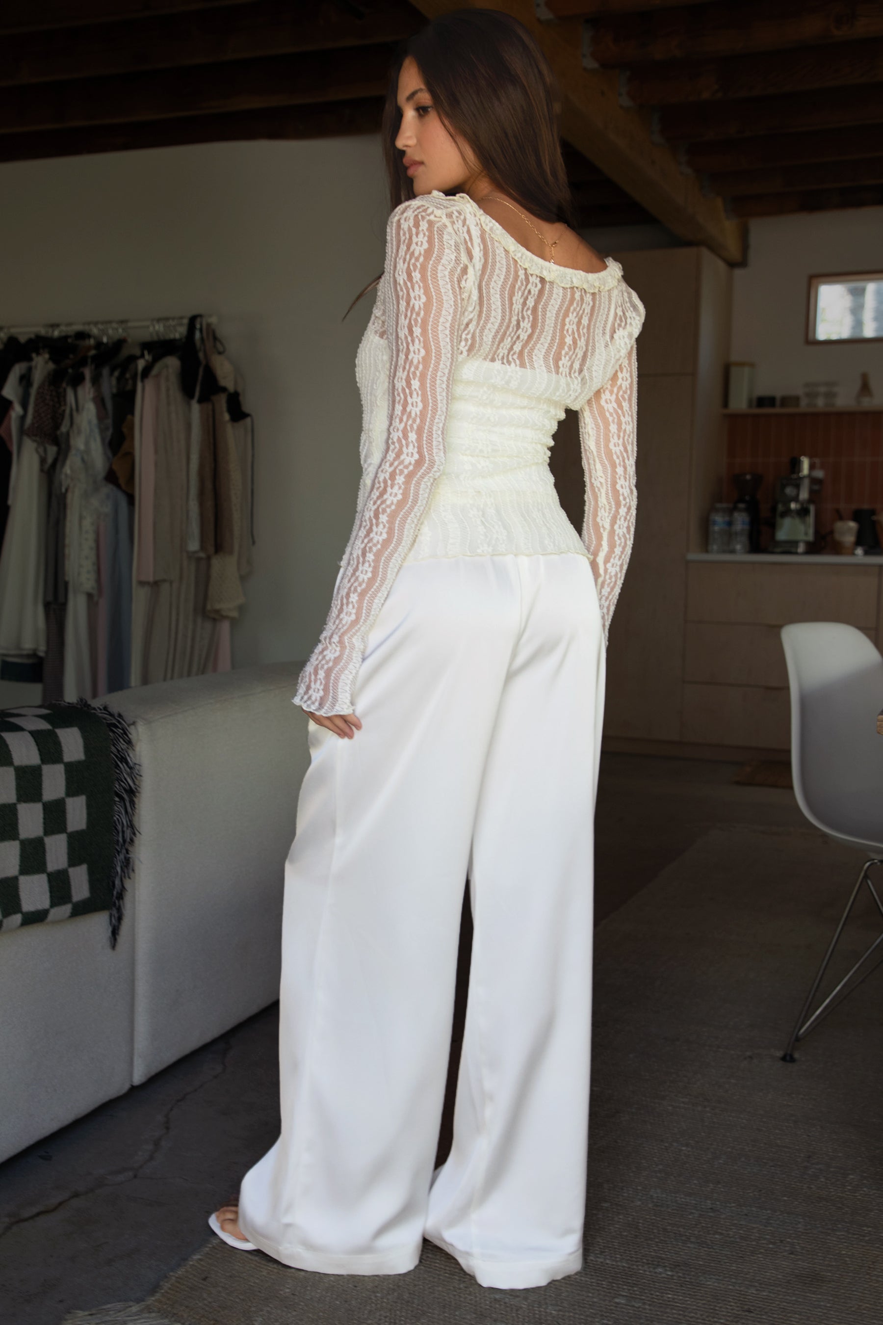 Woman wearing TIC TOC VERONA Satin Pull-On Pants in cream front view with wide leg silhouette paired with a tank top and white lace longs leeve and heels in an indoor setting.