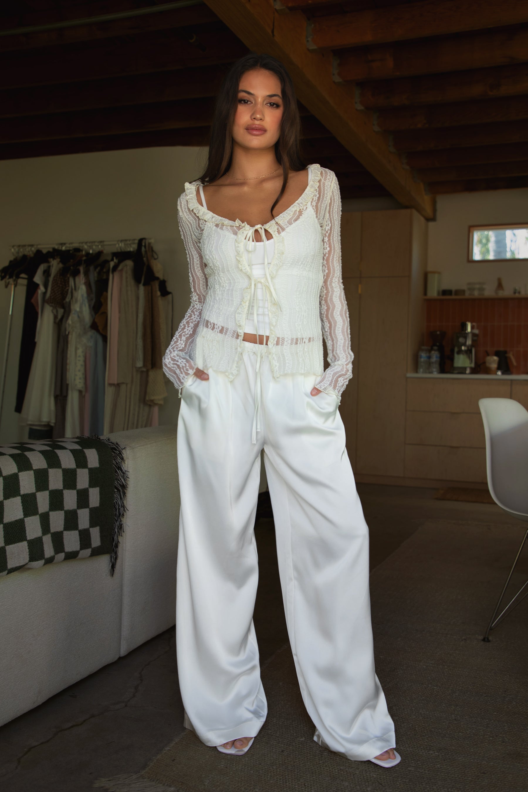 Woman wearing TIC TOC VERONA Satin Pull-On Pants in cream front view with wide leg silhouette paired with a tank top and white lace longs leeve and heels in an indoor setting.
