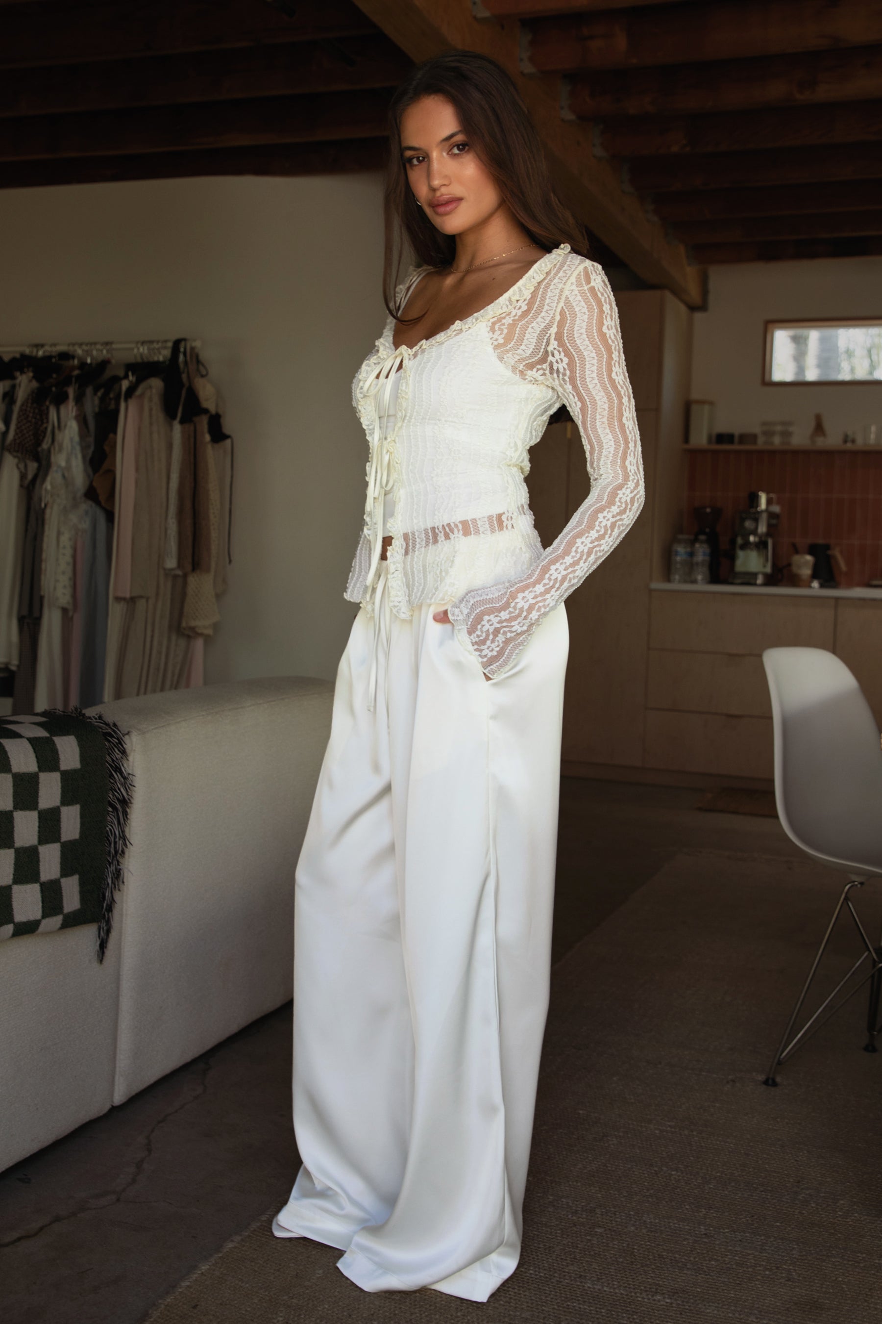 Woman wearing TIC TOC VERONA Satin Pull-On Pants in cream front view with wide leg silhouette paired with a tank top and white lace longs leeve and heels in an indoor setting.