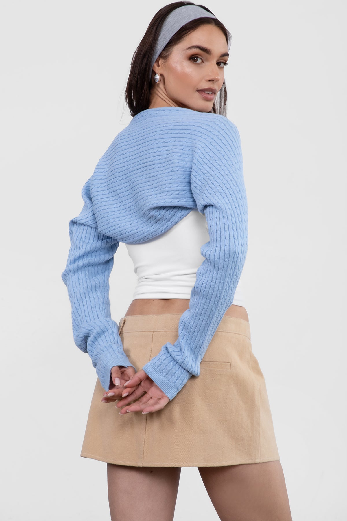 Woman wearing a light blue ribbed sweater over a white top and beige skirt on a white background
