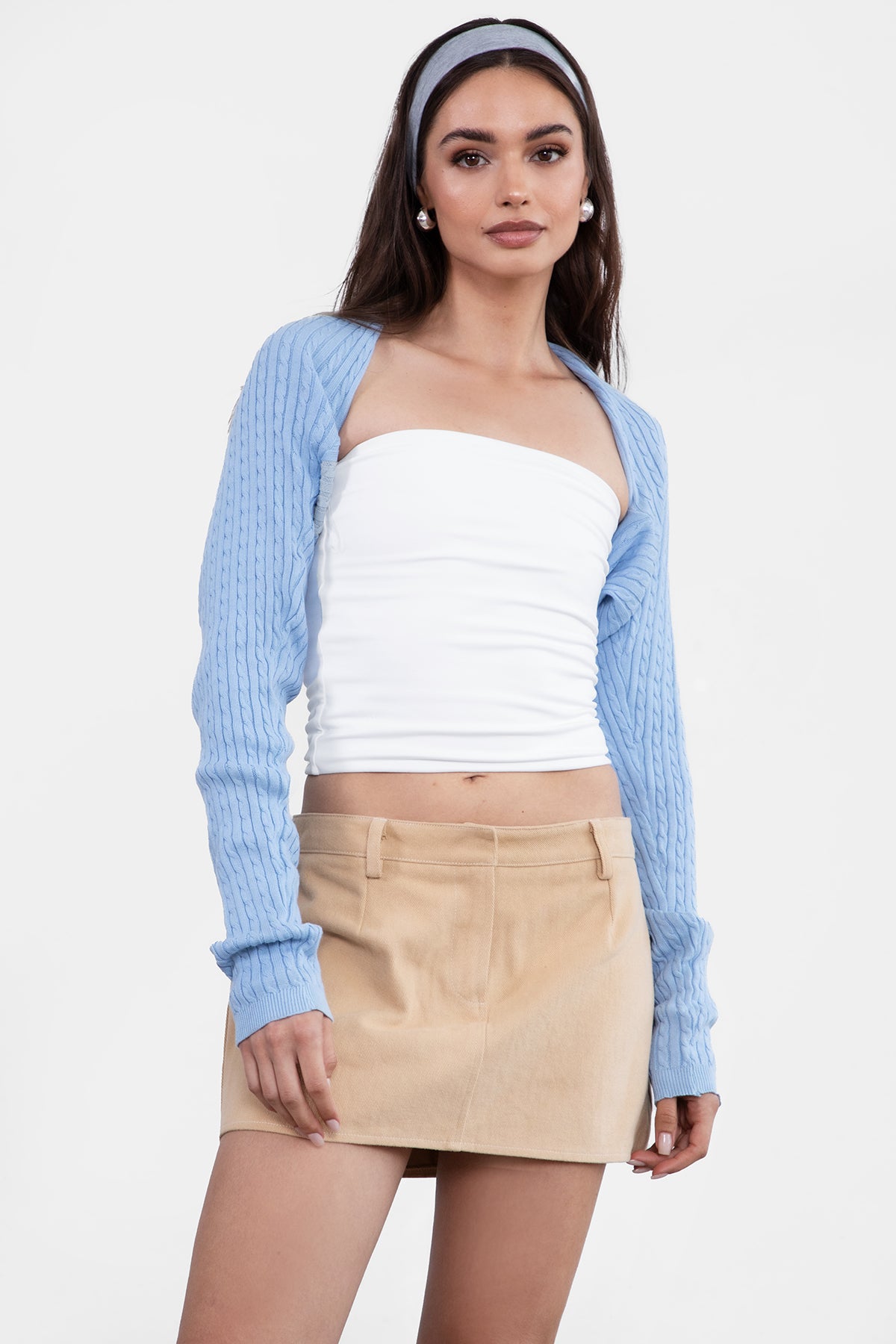 Woman wearing a light blue cardigan, white top, and beige skirt on a white background