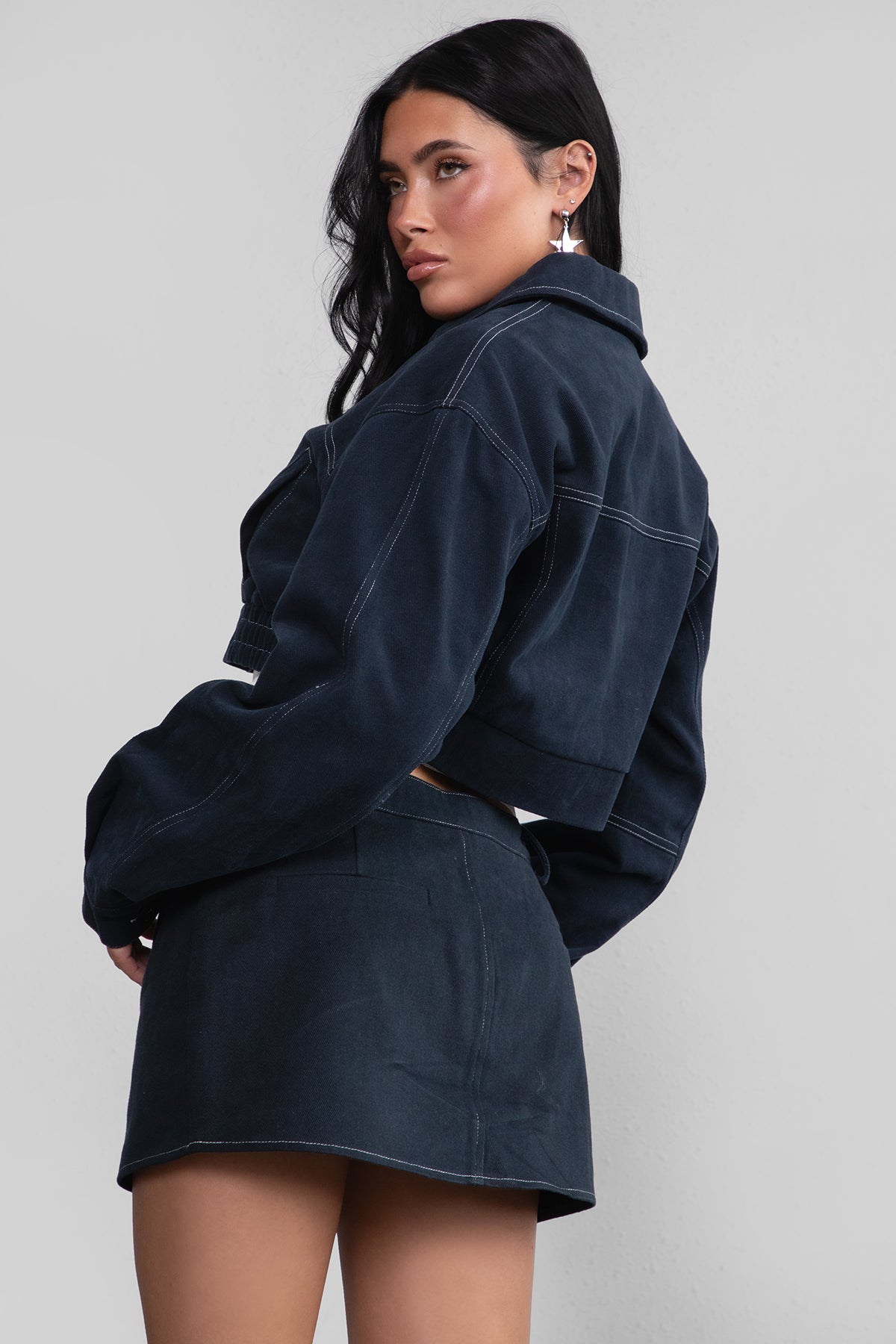 Woman wearing a dark blue denim jacket and skirt on a light gray background