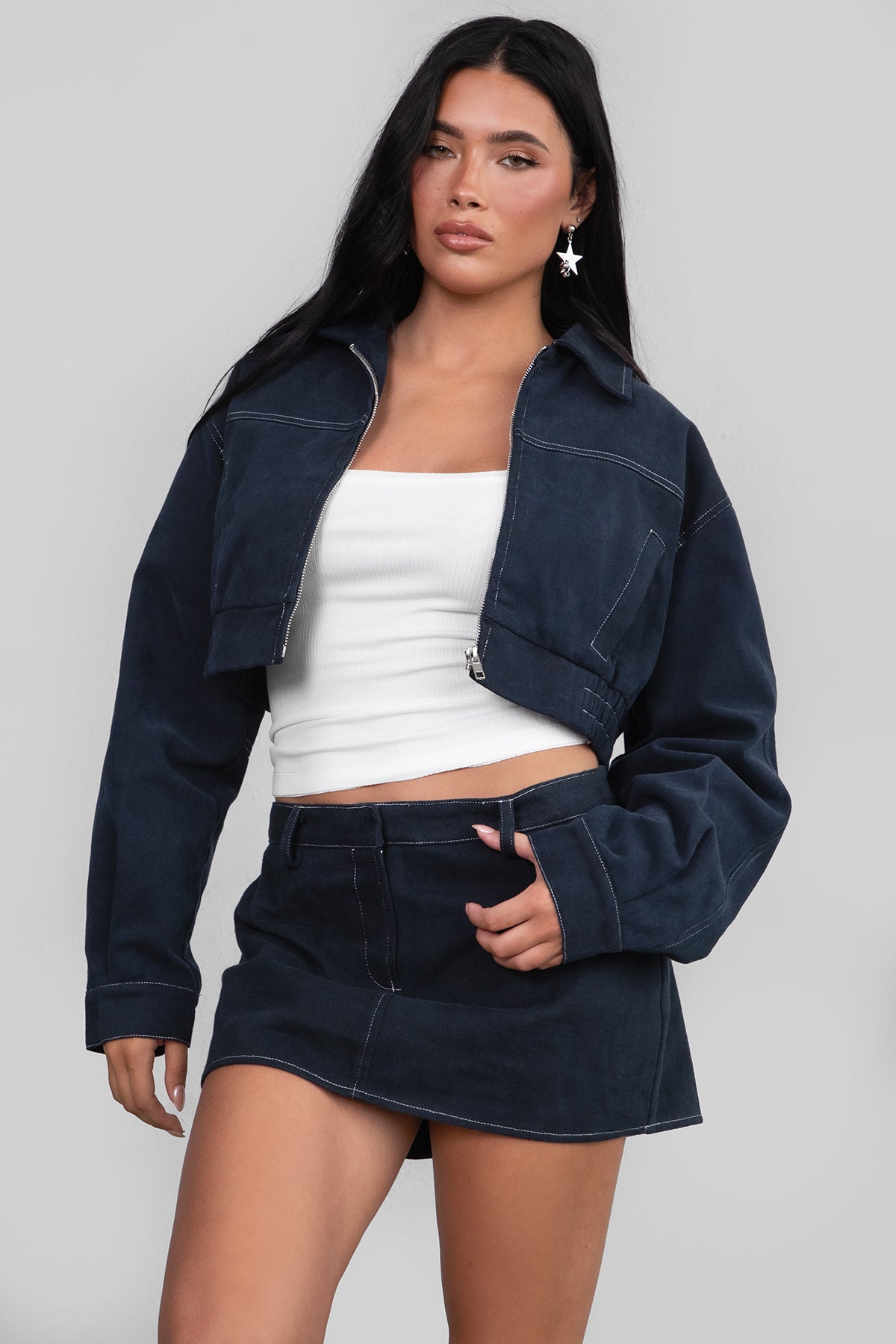 Woman wearing a dark denim jacket and skirt with a white top on a plain background