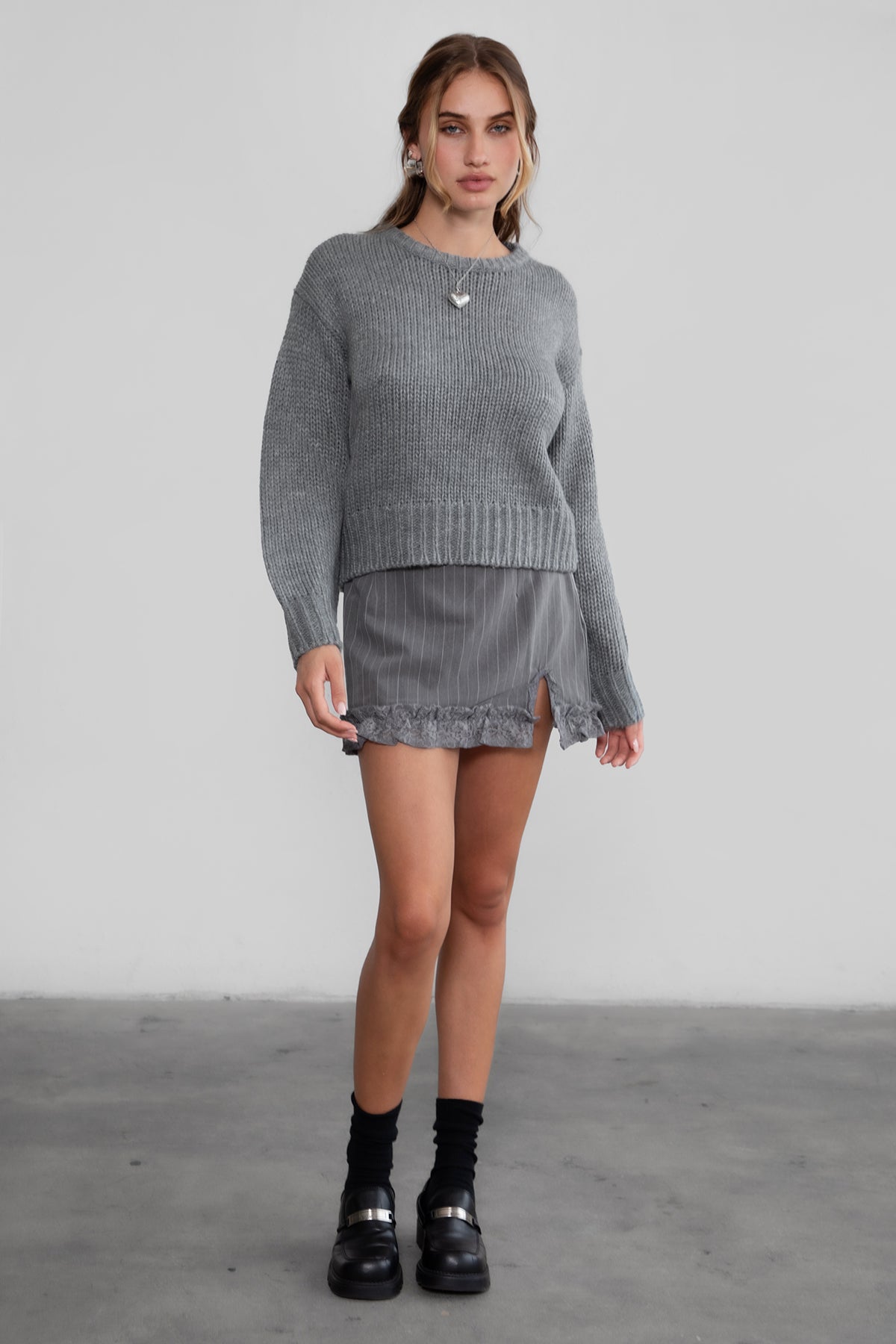 Model wearing TIC TOC KELLY Ribbed Knit Sweater in grey Styled fall outfit with striped mini skirt and loafers. 