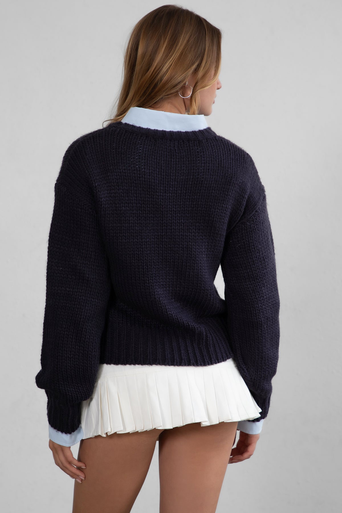 A woman wearing a navy ribbed knit sweater and white denim mini skirt 