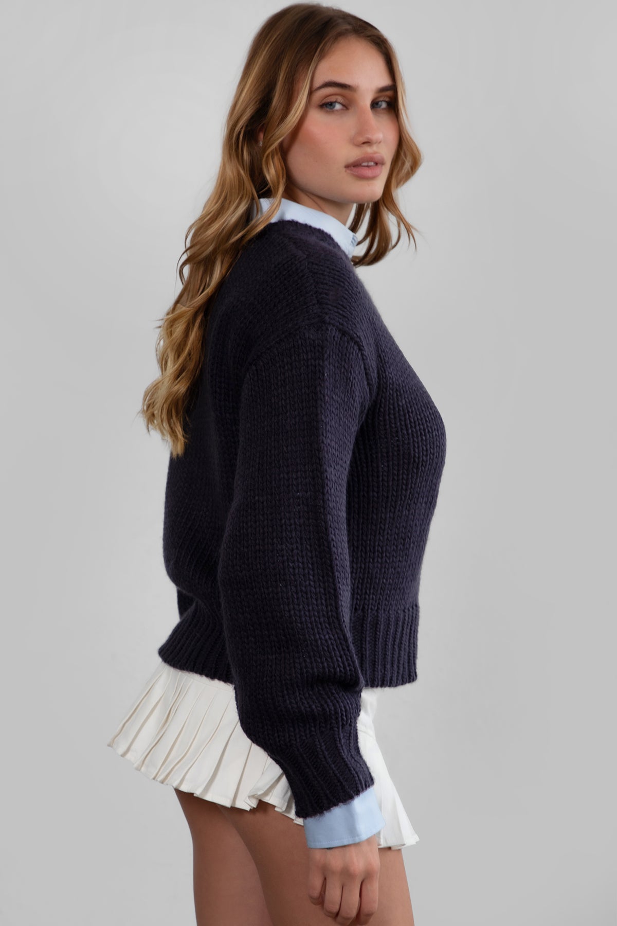 A woman wearing a navy ribbed knit sweater and white denim mini skirt 