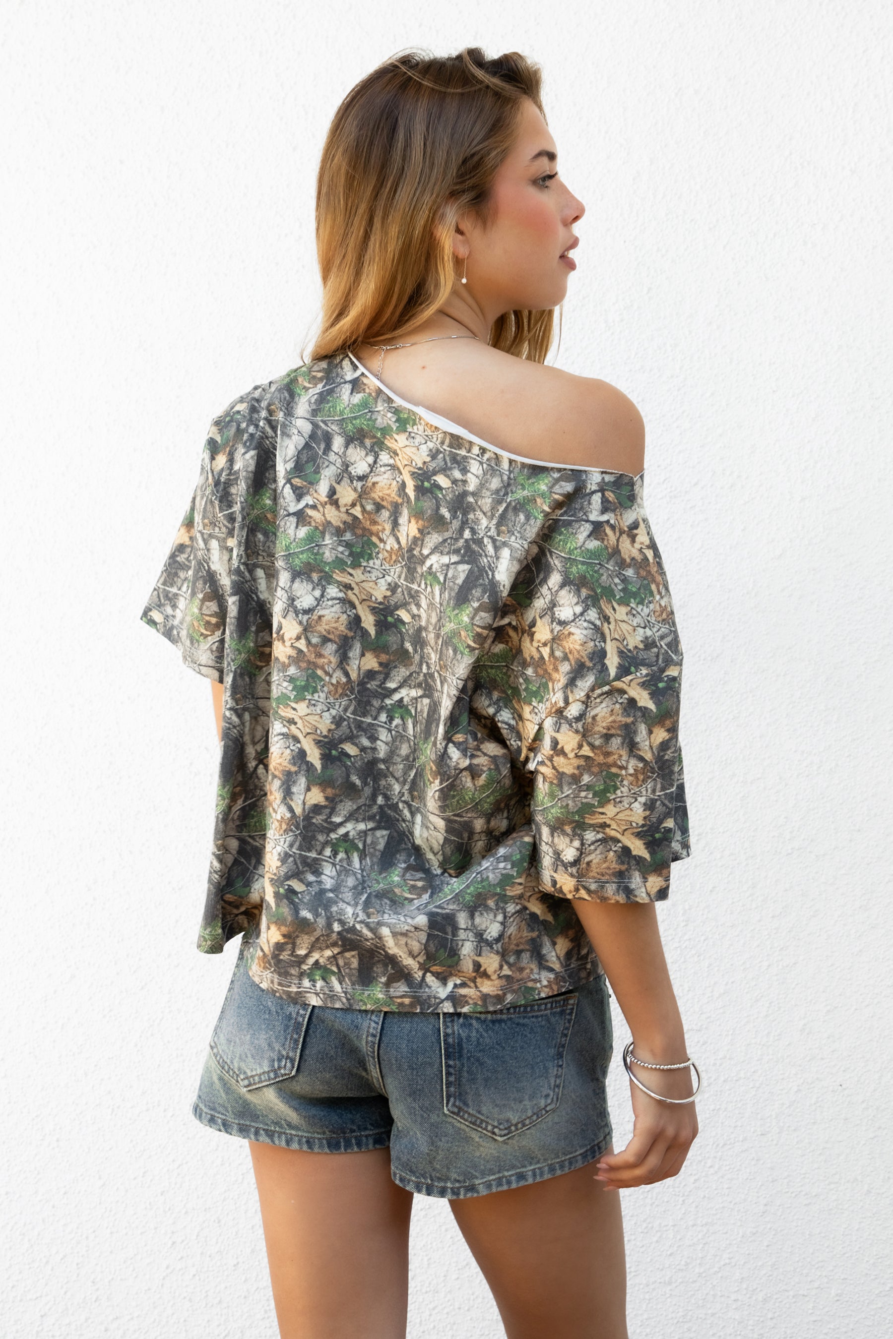 Woman wearing BAYOU camo print oversized one shoulder T-shirt featuring soft washed cotton jersey fabric, oversized slouchy silhouette, asymmetrical neckline, woodland camo print, and loose short sleeves for relaxed off-duty styling.