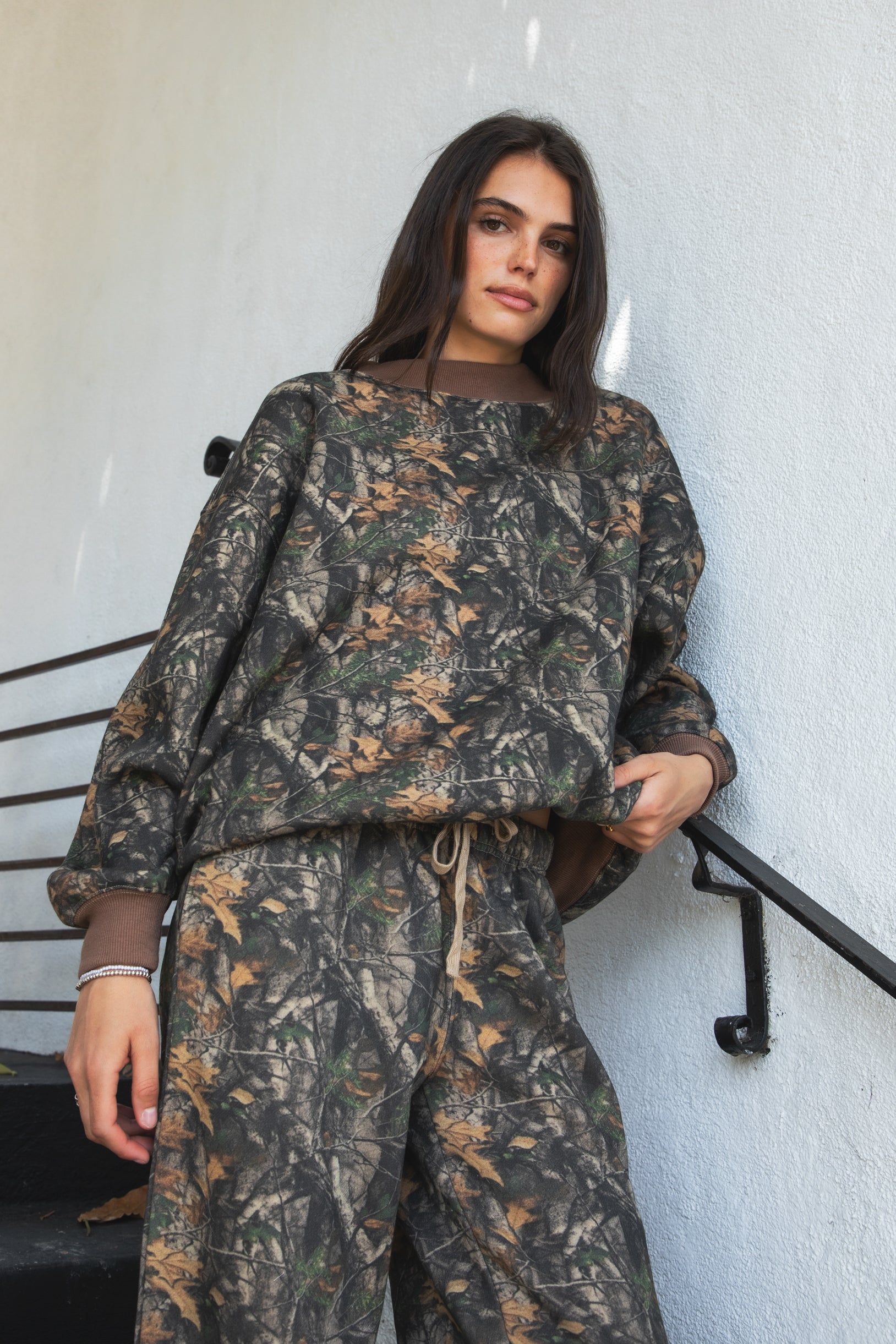 Woman wearing BAYOU dark woodland camo mock neck sweatshirt featuring soft cloud fleece fabric, allover woodland camo print, wide mock neckline with contrast ribbed trim, dropped shoulder relaxed silhouette, oversized fit, long sleeves, and contrast ribbed cuffs and hem.