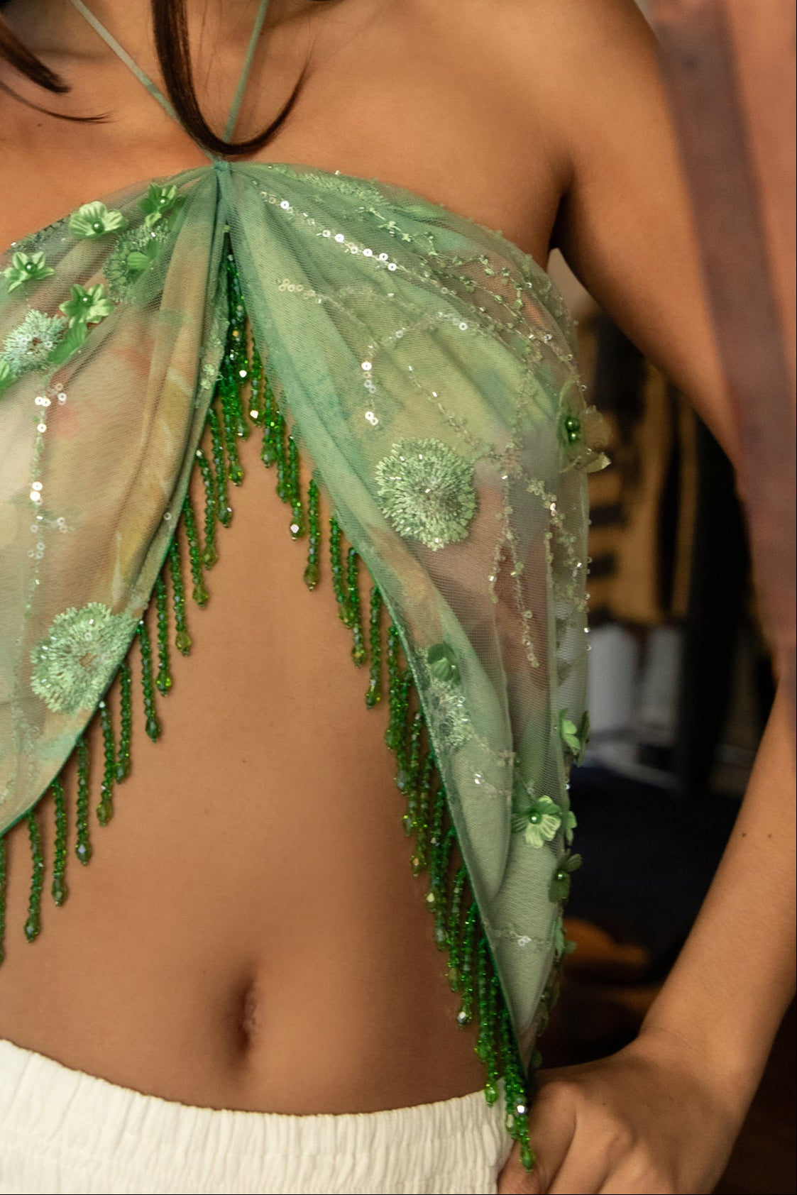 Woman wearing TIC TOC TL31629-SERAYA SERAYA beaded tassel embellished mesh halter scarf top featuring sheer embroidered mesh fabric with floral appliqué and sequin accents, beaded tassel fringe along the hem, halter neck tie closure, and an open back with adjustable tie, styled over a simple bralette and low-rise bottoms for a bold festival and resort-ready statement look.