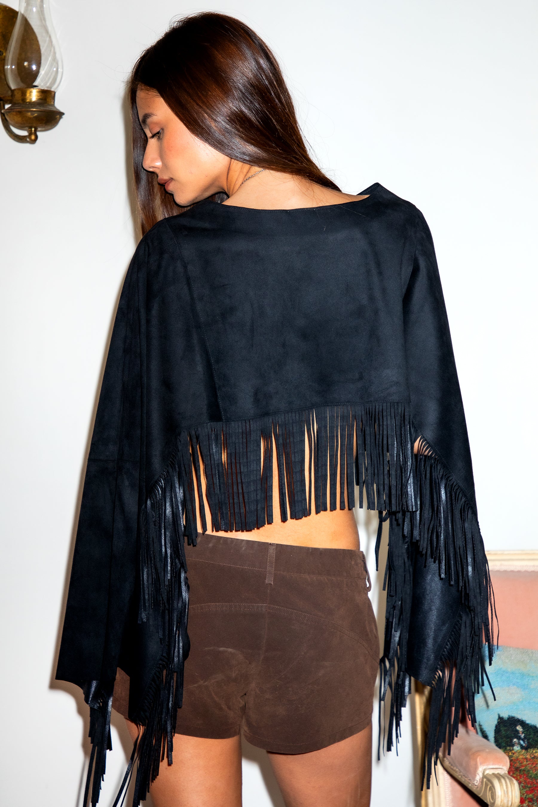 Woman wearing TIC TOC TL31825 STALLION faux suede fringe poncho featuring a cropped cape silhouette, drop shoulder relaxed fit, long fringe tassel detailing along the hem and sleeves, and a soft western-inspired faux suede texture, styled over a fitted top with denim bottoms for a rodeo festival look.