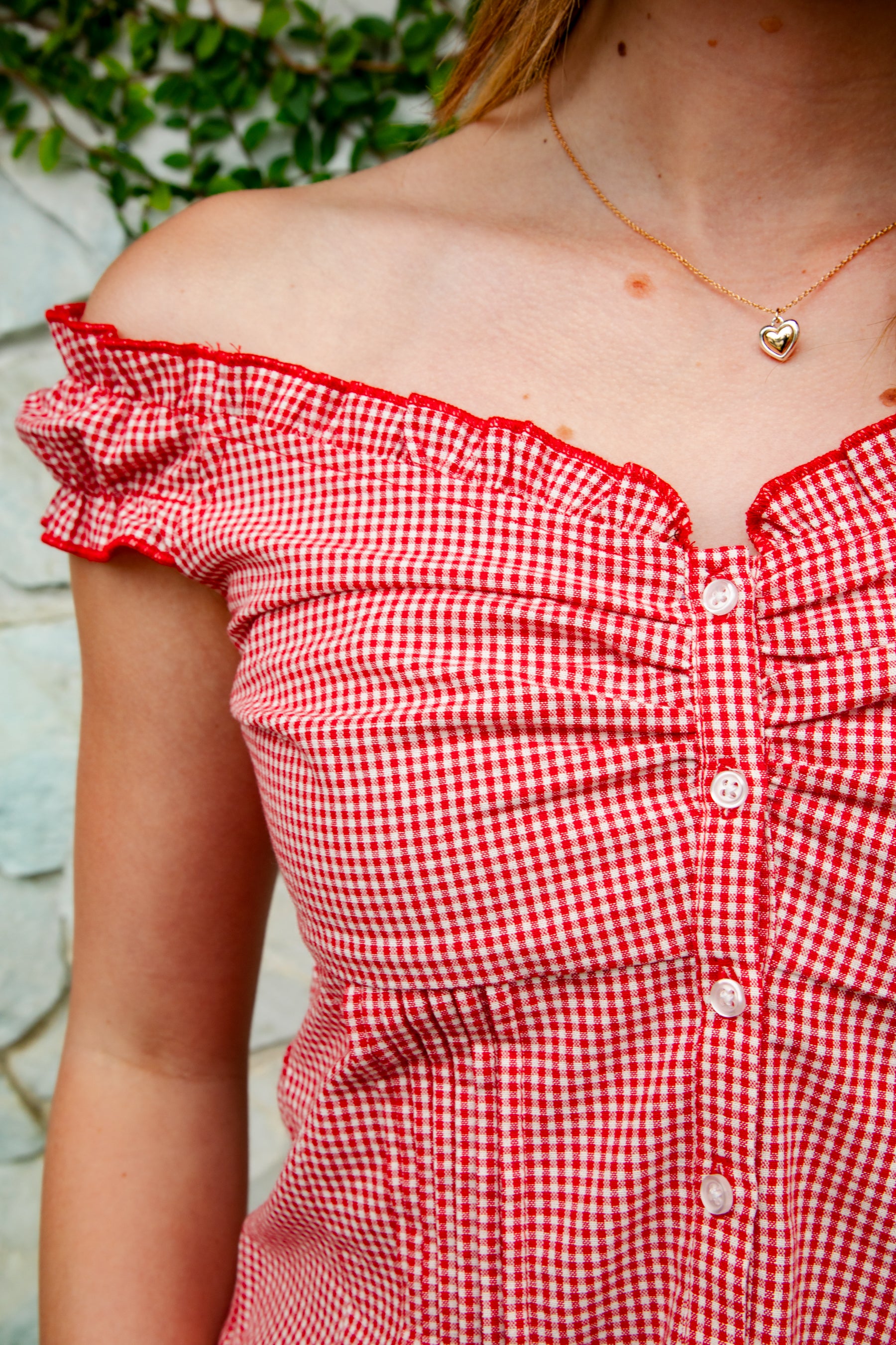 Woman wearing MAREN gingham off shoulder ruffle cap sleeve top featuring a soft ruffle neckline, ruched bust detail, functional button front, smocked back panel, ruffled peplum hem, and lightweight cotton gingham fabric for feminine summer styling.