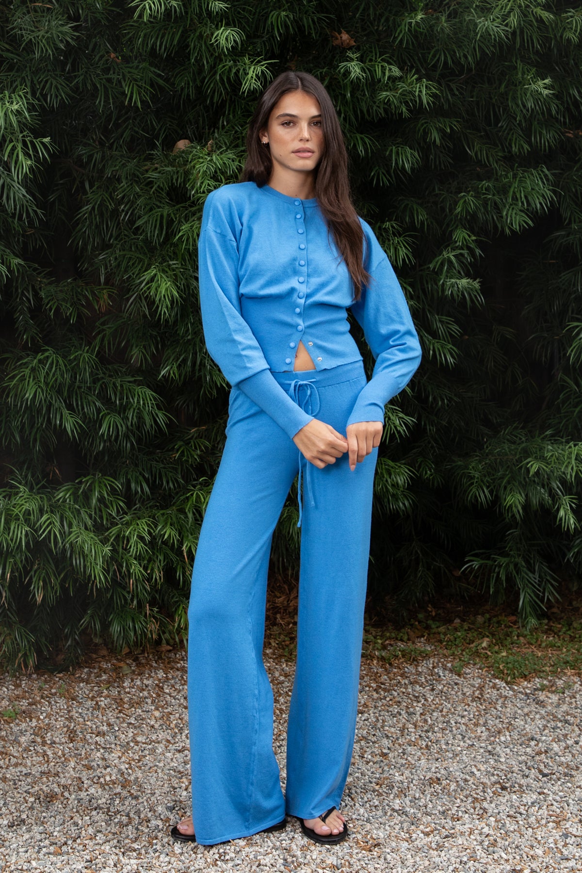 Woman wearing AZUREE button front cardigan and wide leg pants set featuring soft stretch sweater knit fabric, cropped cardigan with round neckline, covered button front closure, relaxed dropped shoulders, long sleeves with extended ribbed cuffs, fitted ribbed waistband, and matching high waisted pants with adjustable drawstring waist and relaxed full length wide leg silhouette.